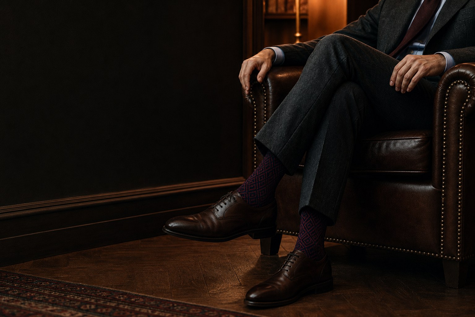 A man in tailored trousers wearing deep burgundy and navy bamboo dress socks with brown Oxford shoes