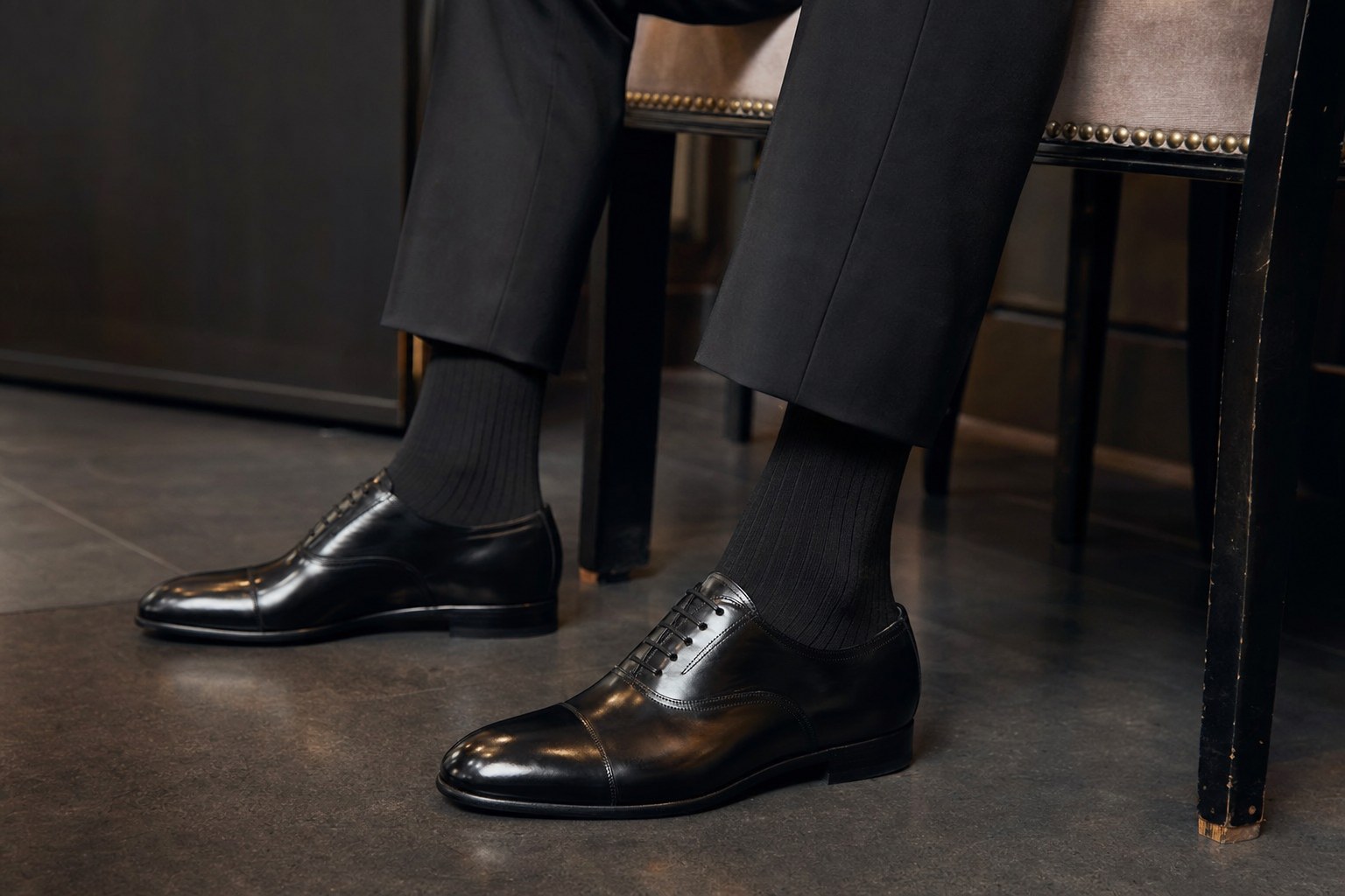 A seated tuxedo wearer with black dress socks covering the leg above polished black shoes