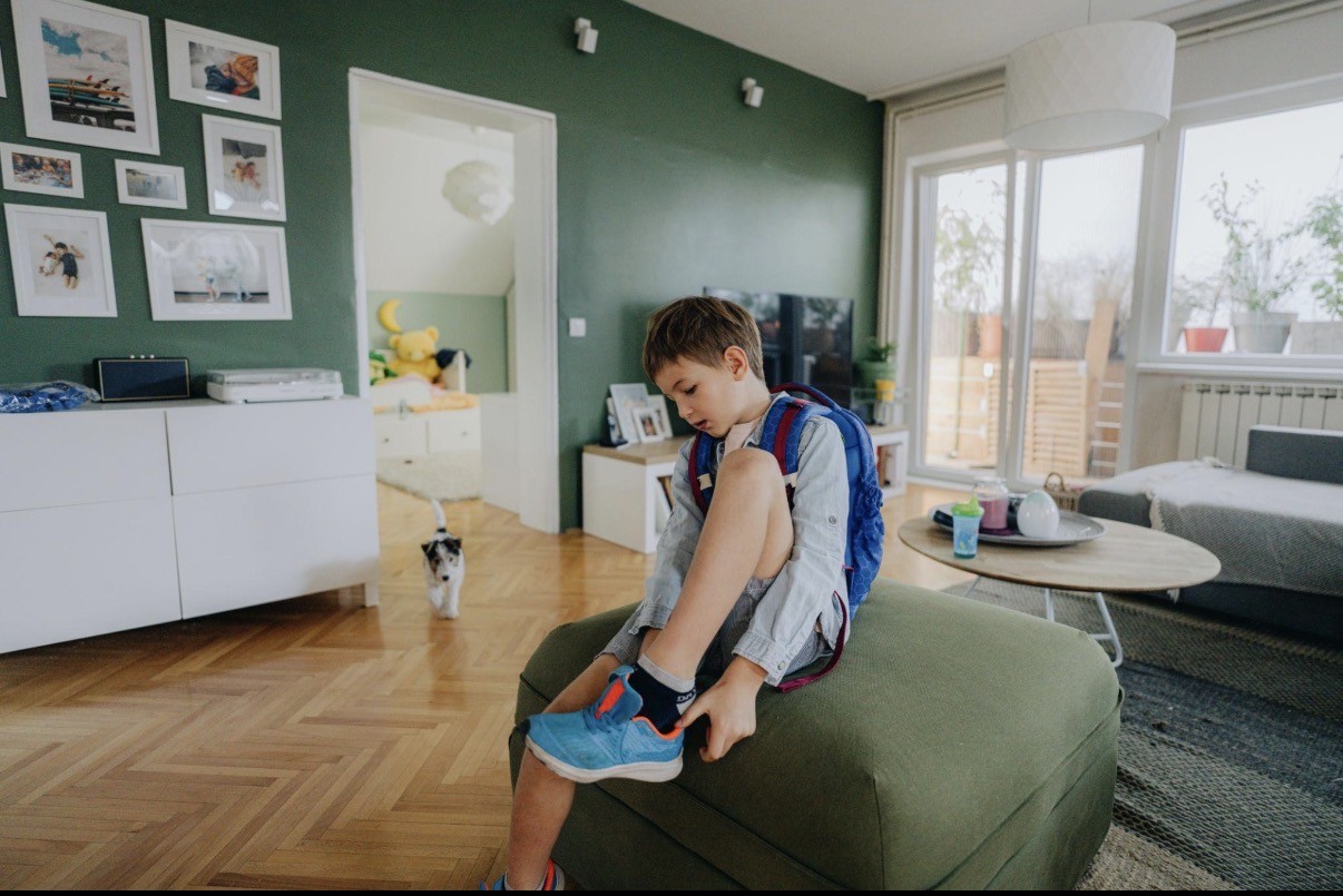 A child putting on a shoe while getting ready with a backpack