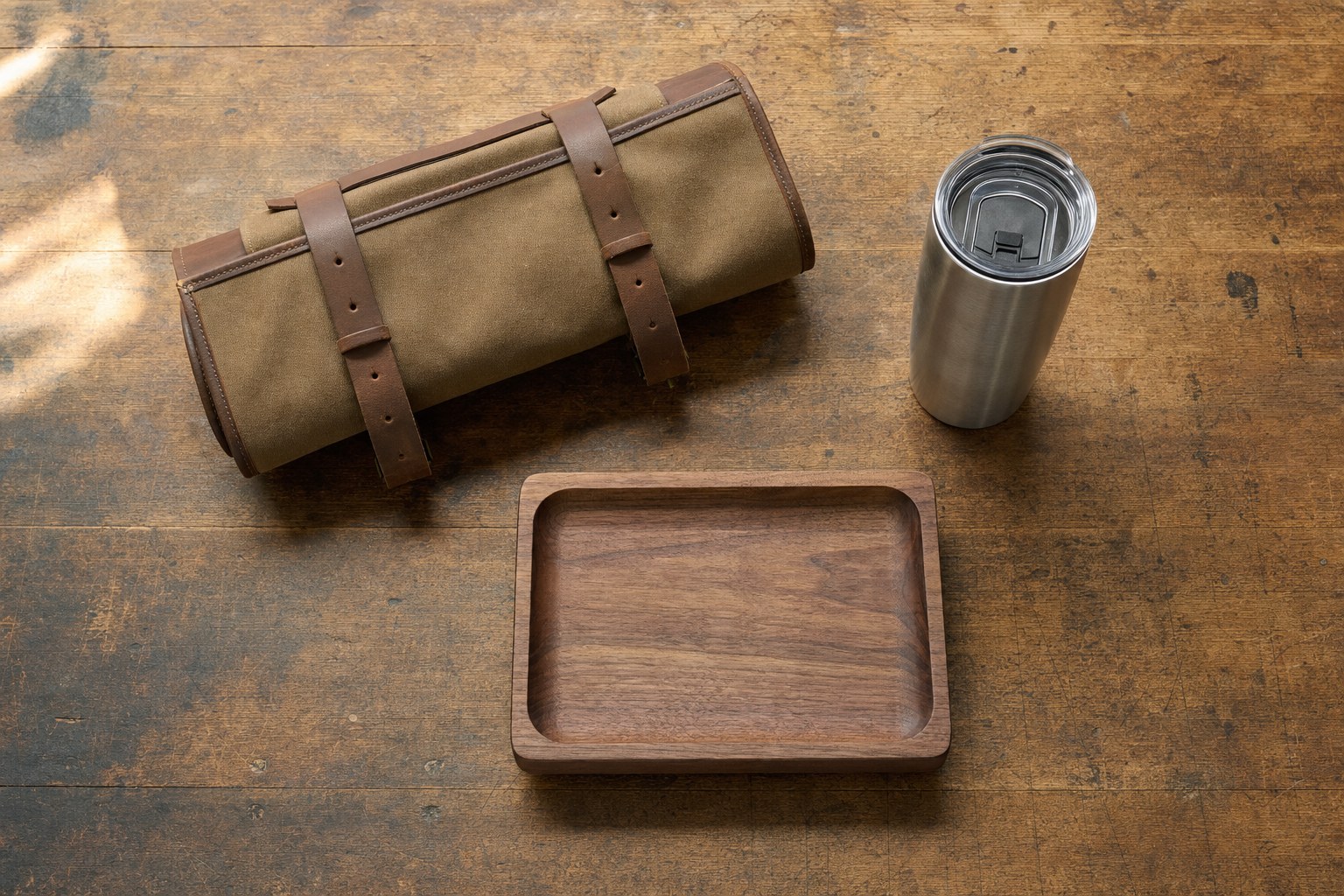 Canvas tool roll, stainless tumbler, and walnut valet tray arranged on a wood workbench