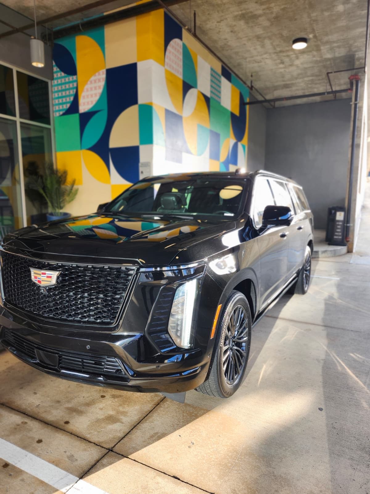 Black Cadillac SUV beside a colorful mural