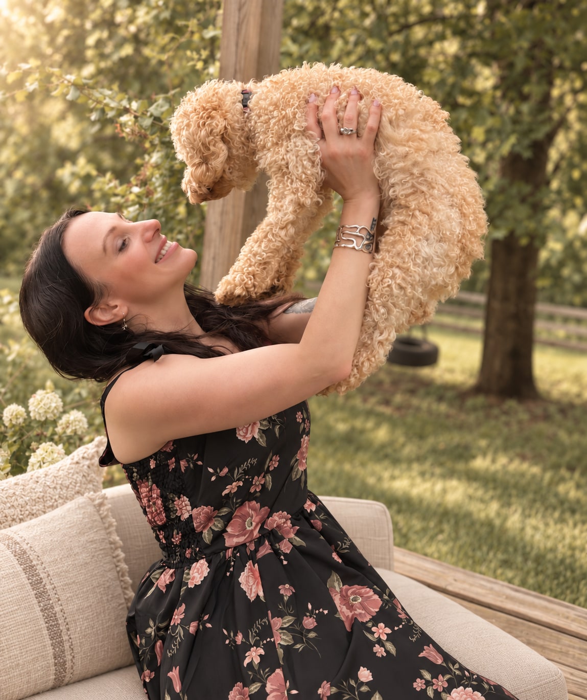 A woman lifting her small curly-haired dog outdoors