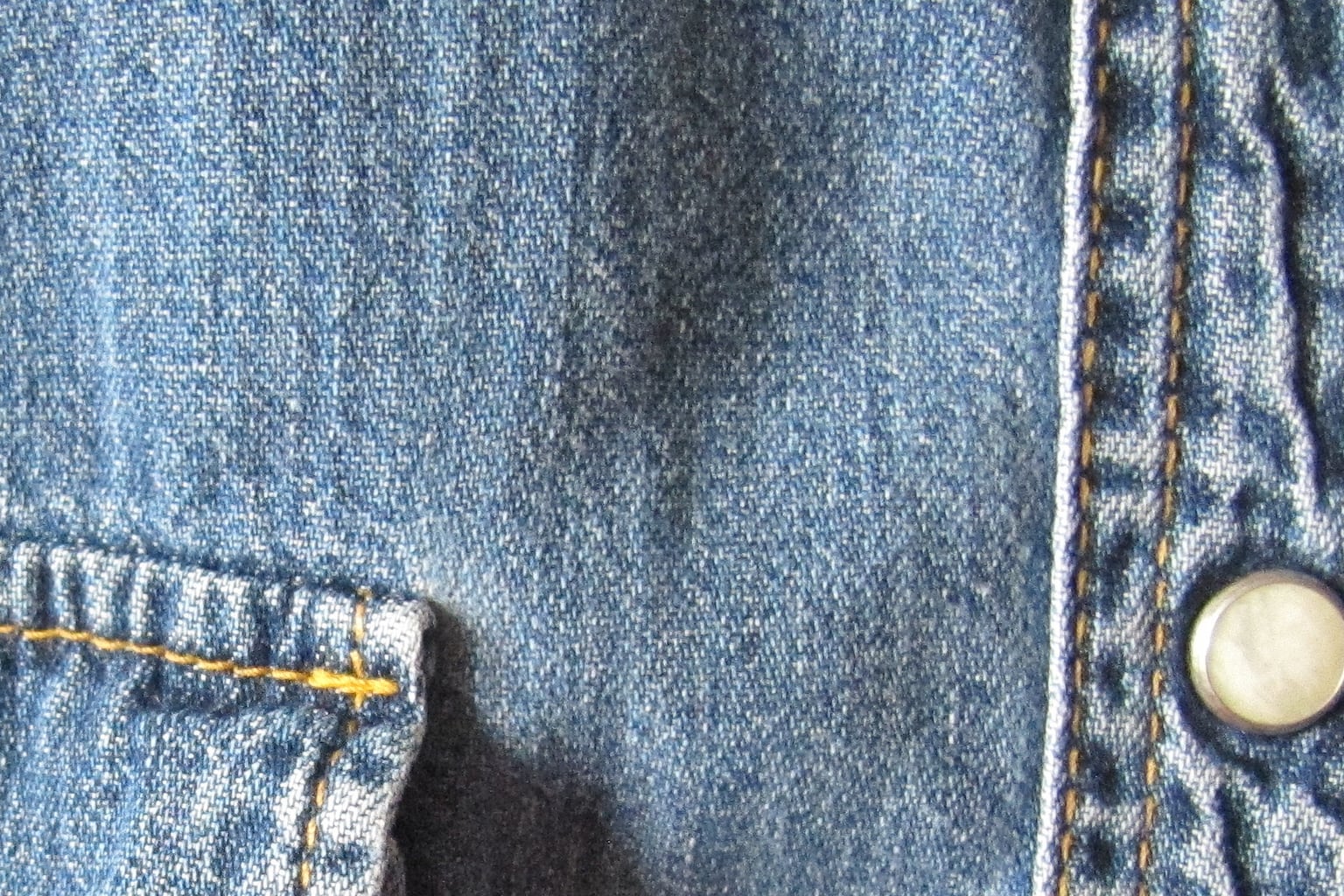 Close detail of the button placket and faded blue denim texture on a work shirt