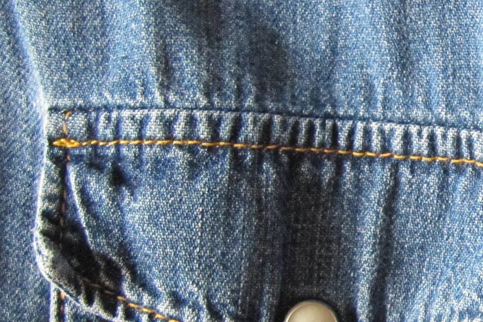 Detailed view of a denim work shirt pocket, stitching and snap