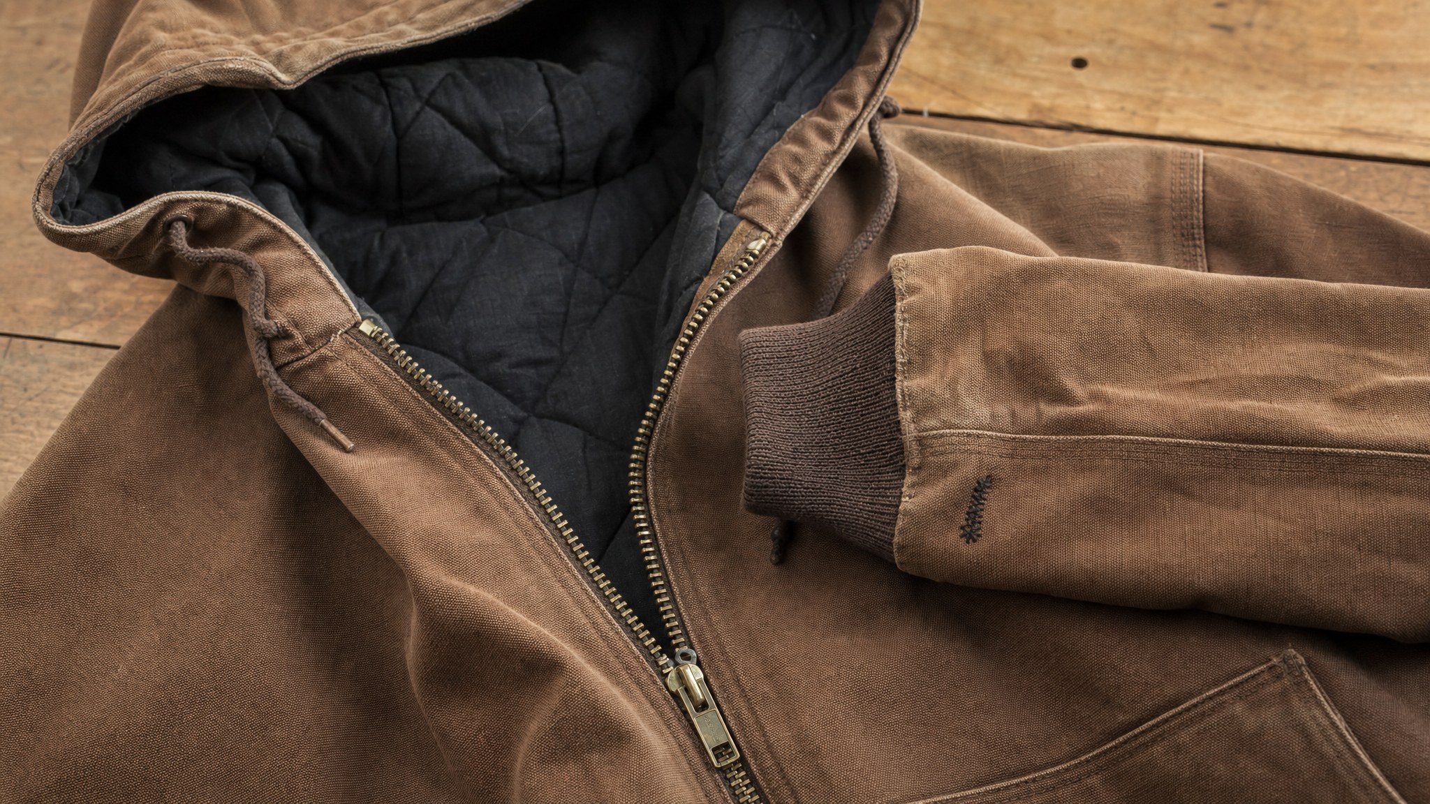 Close view of a brown hooded canvas work jacket showing zipper, quilted lining and cuff condition