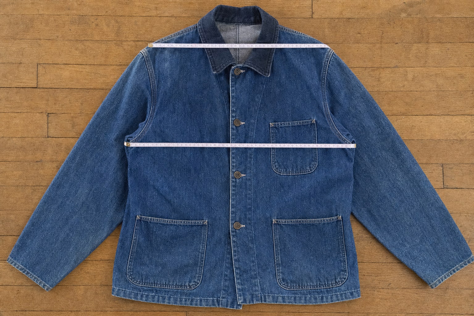 Vintage denim chore jacket laid flat with measuring tapes across the shoulders and chest