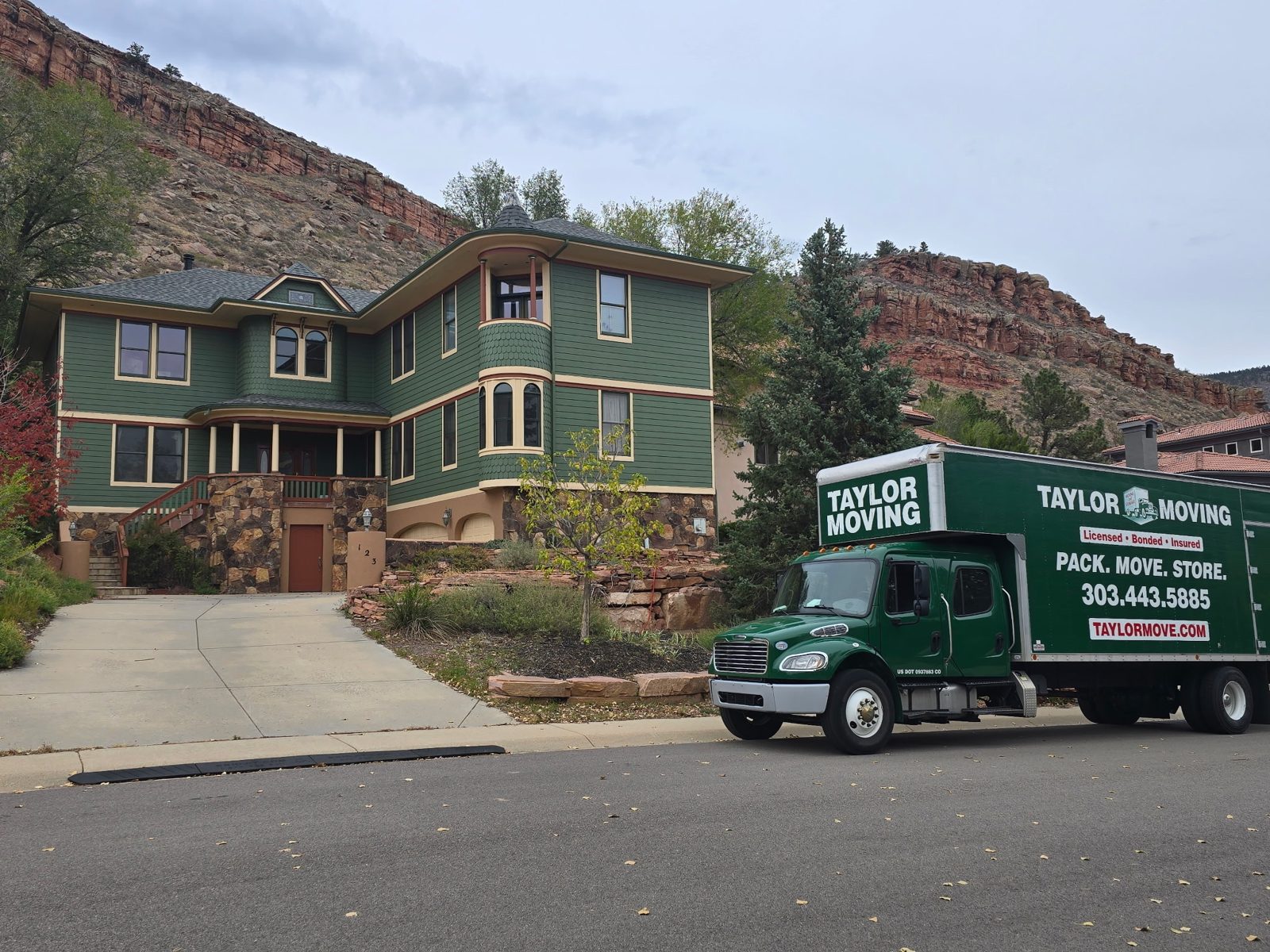 Taylor Moving truck beside a green house beneath red rock cliffs