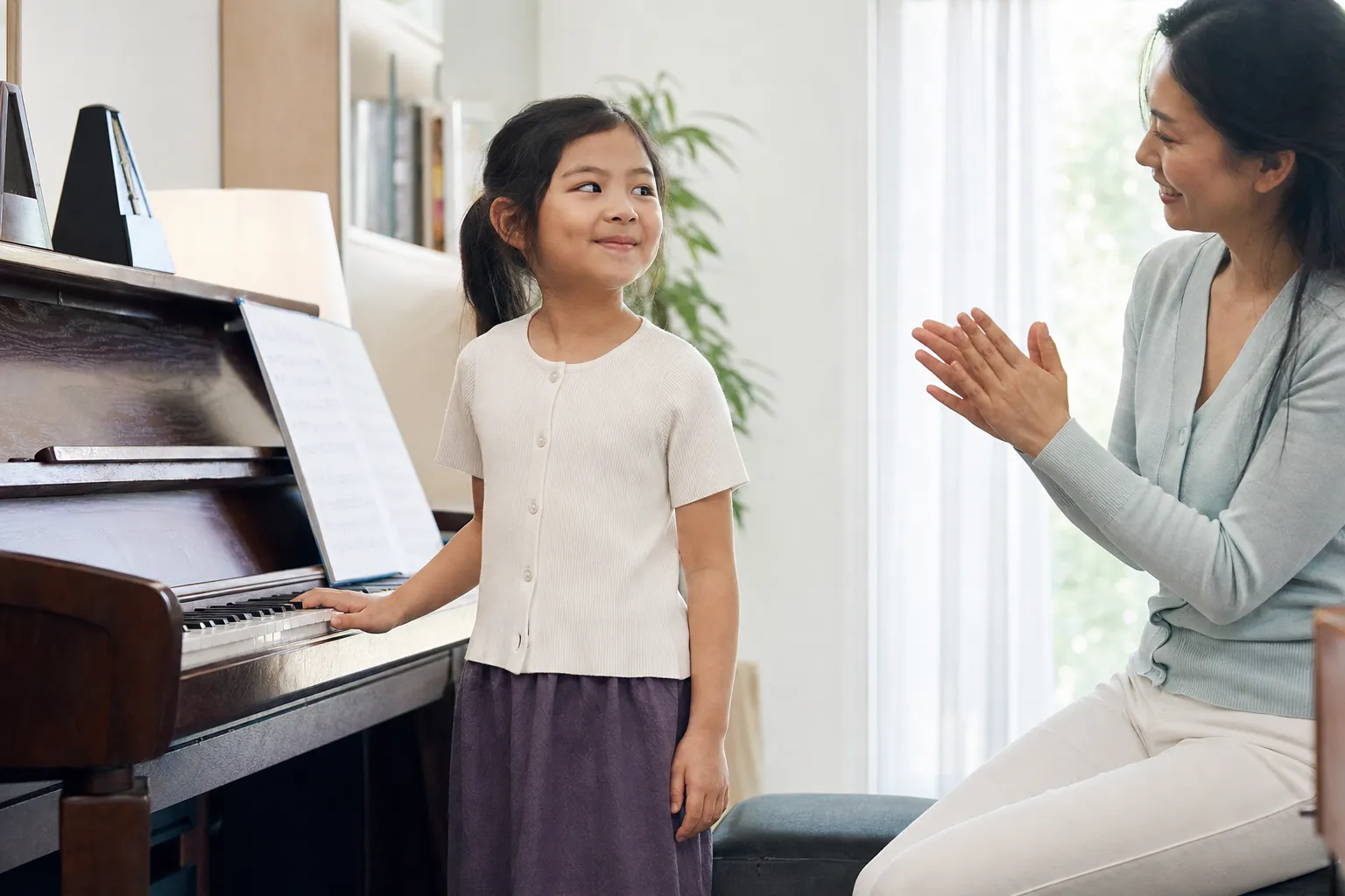 young piano student smiling after playing a short piece while a teacher applauds