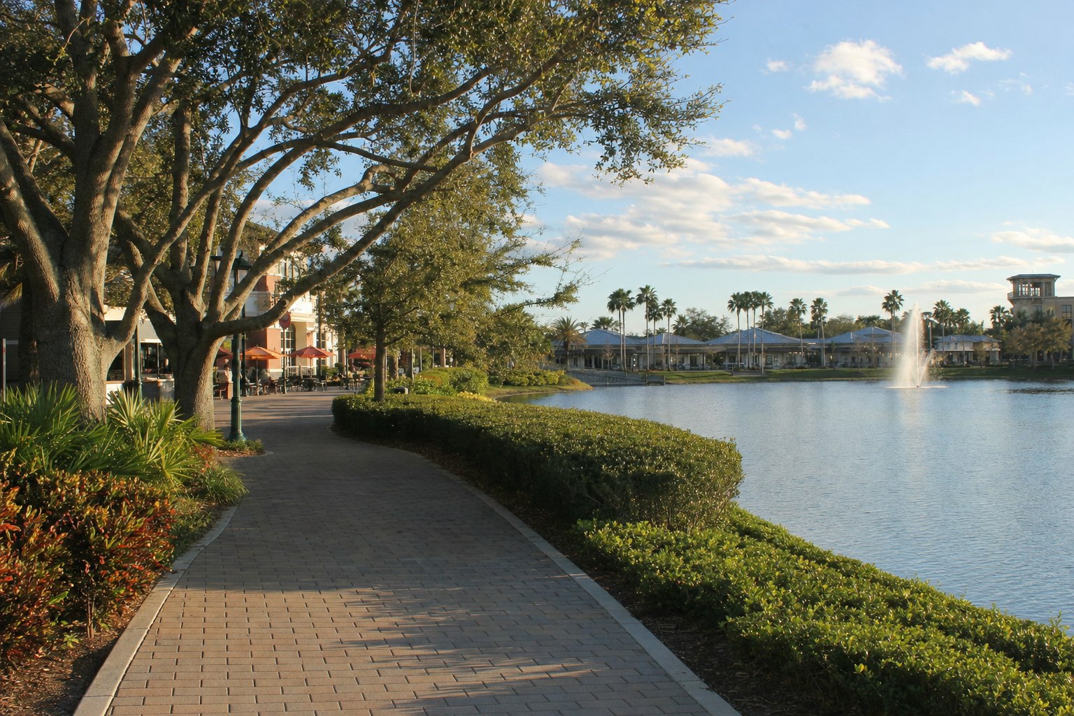 Illustrative Florida town-center walkway beside a lake with outdoor seating in the distance