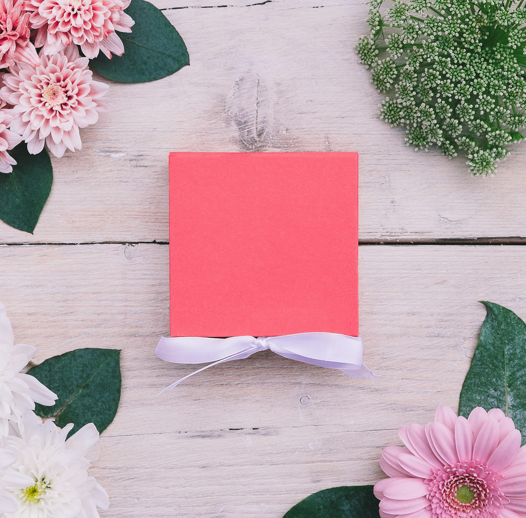 Blank card beside pink flowers on a warm wooden table