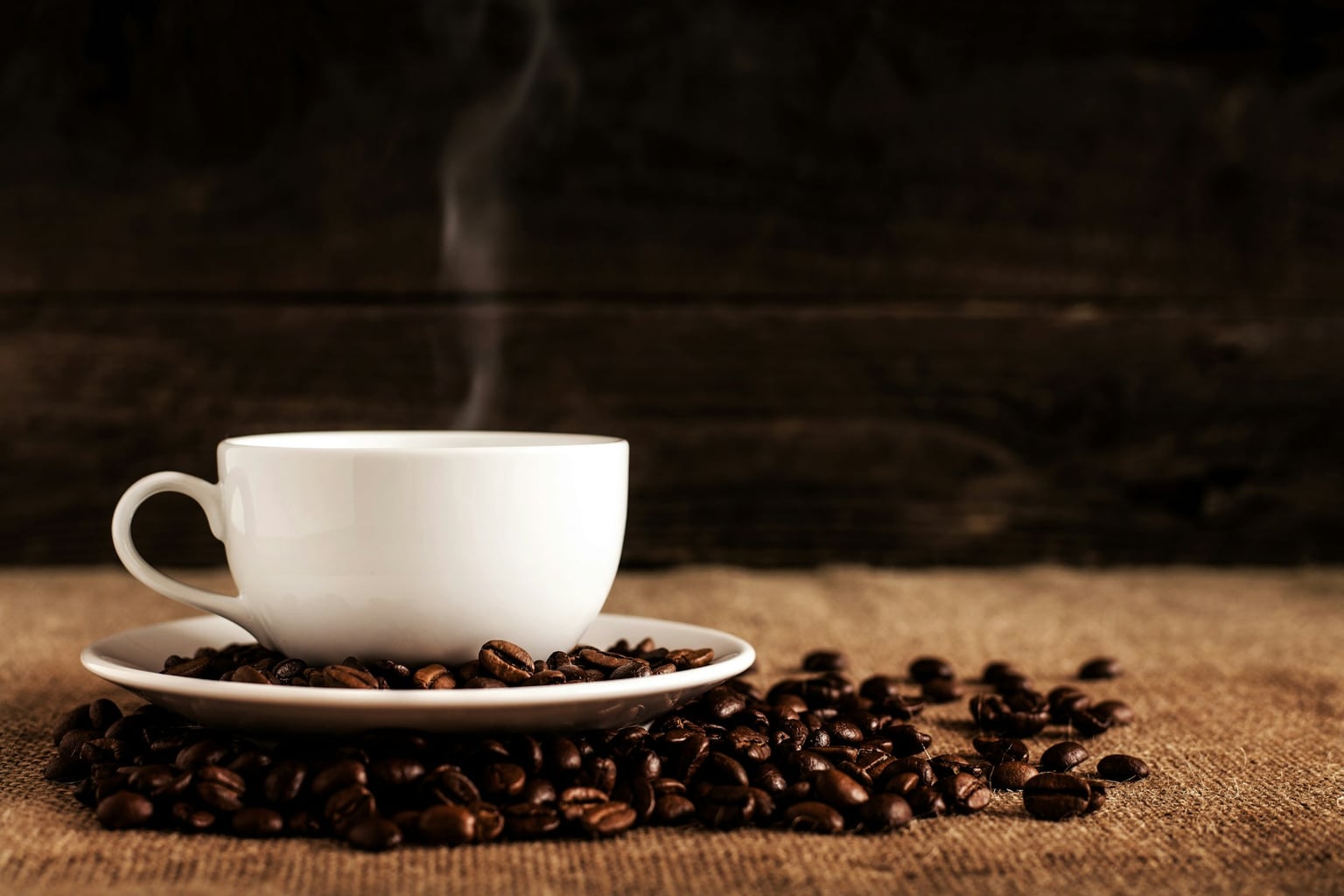 Steaming white coffee cup with coffee beans on a wooden table