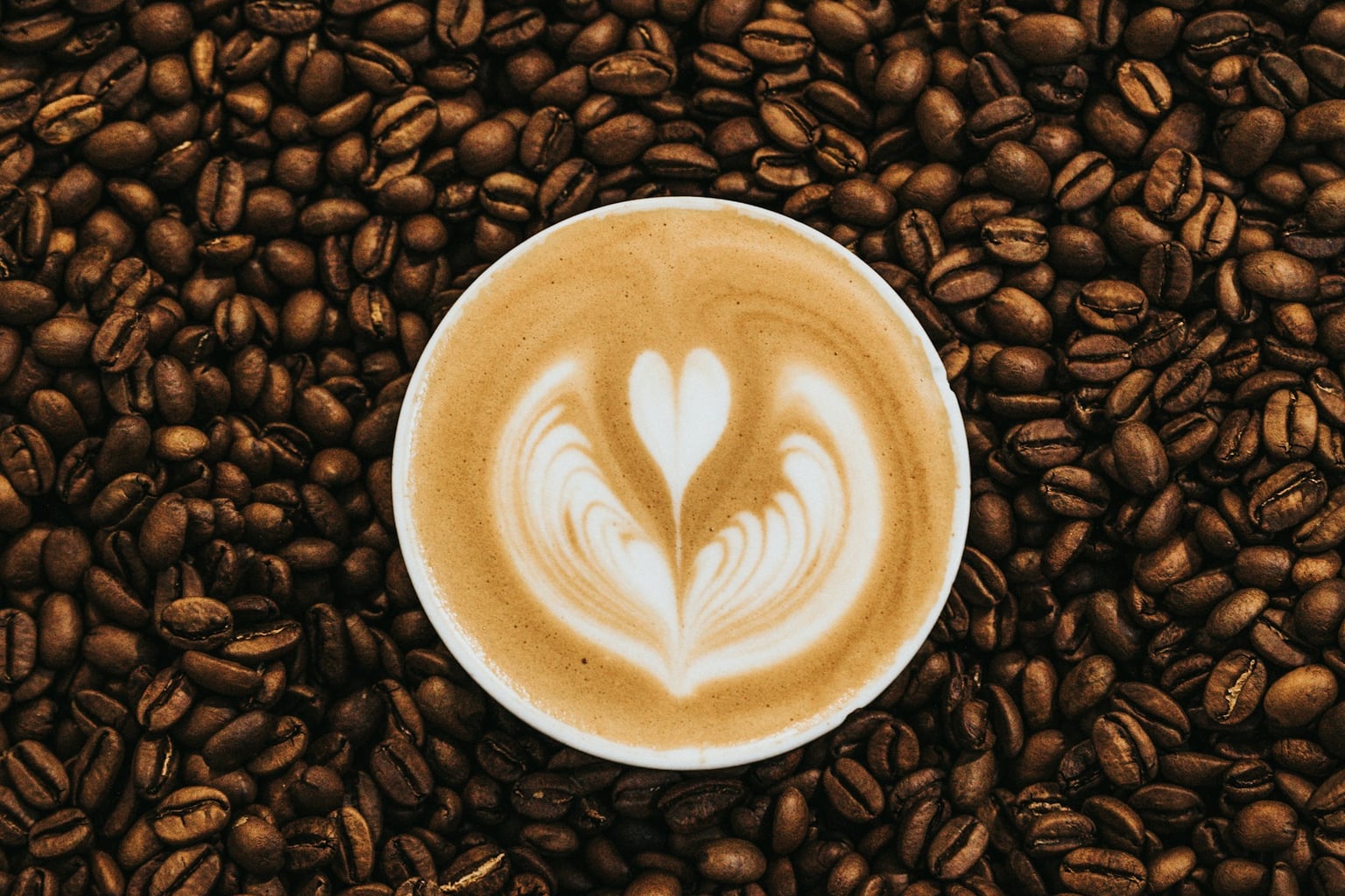 White coffee cup on a wood table surrounded by coffee beans