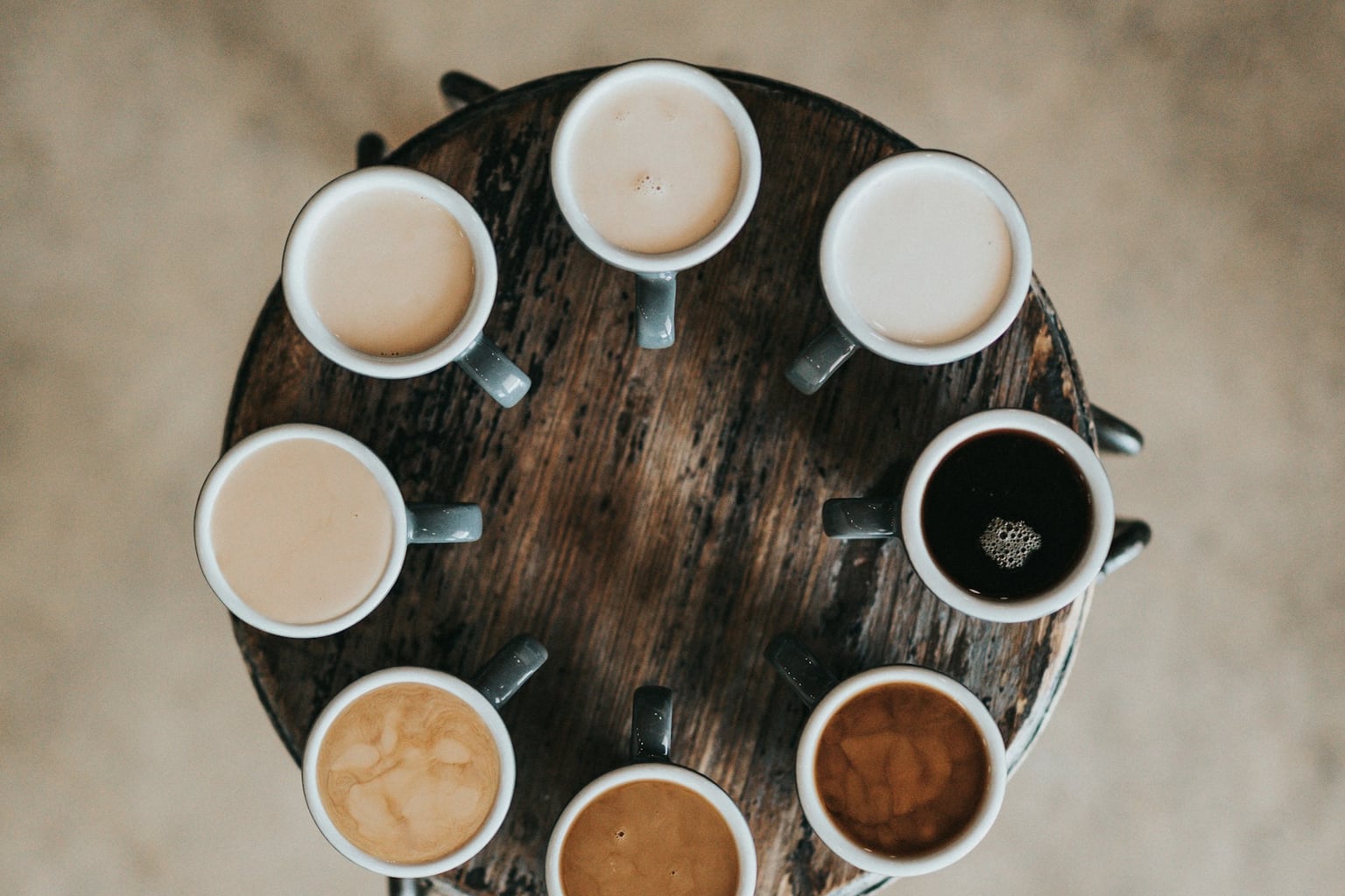Several cups of coffee arranged on a round wood table