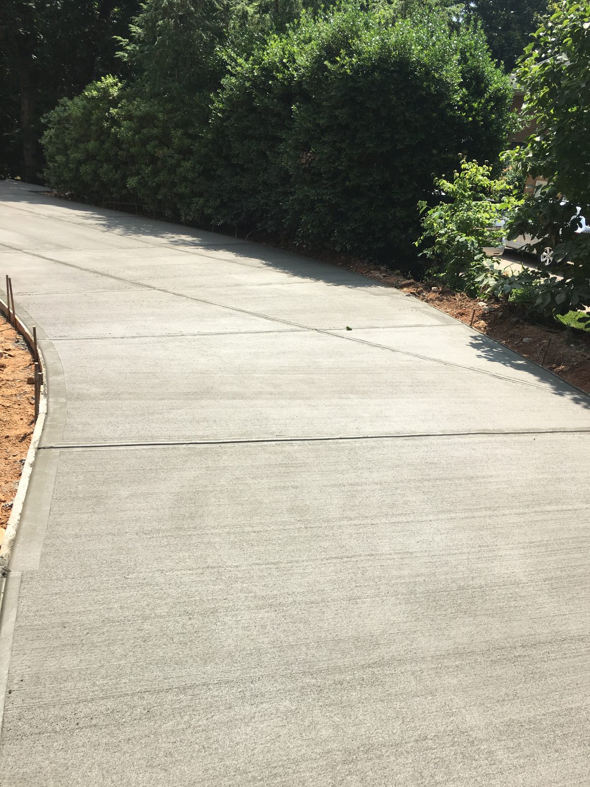 Finished concrete driveway curving beside a green hedge