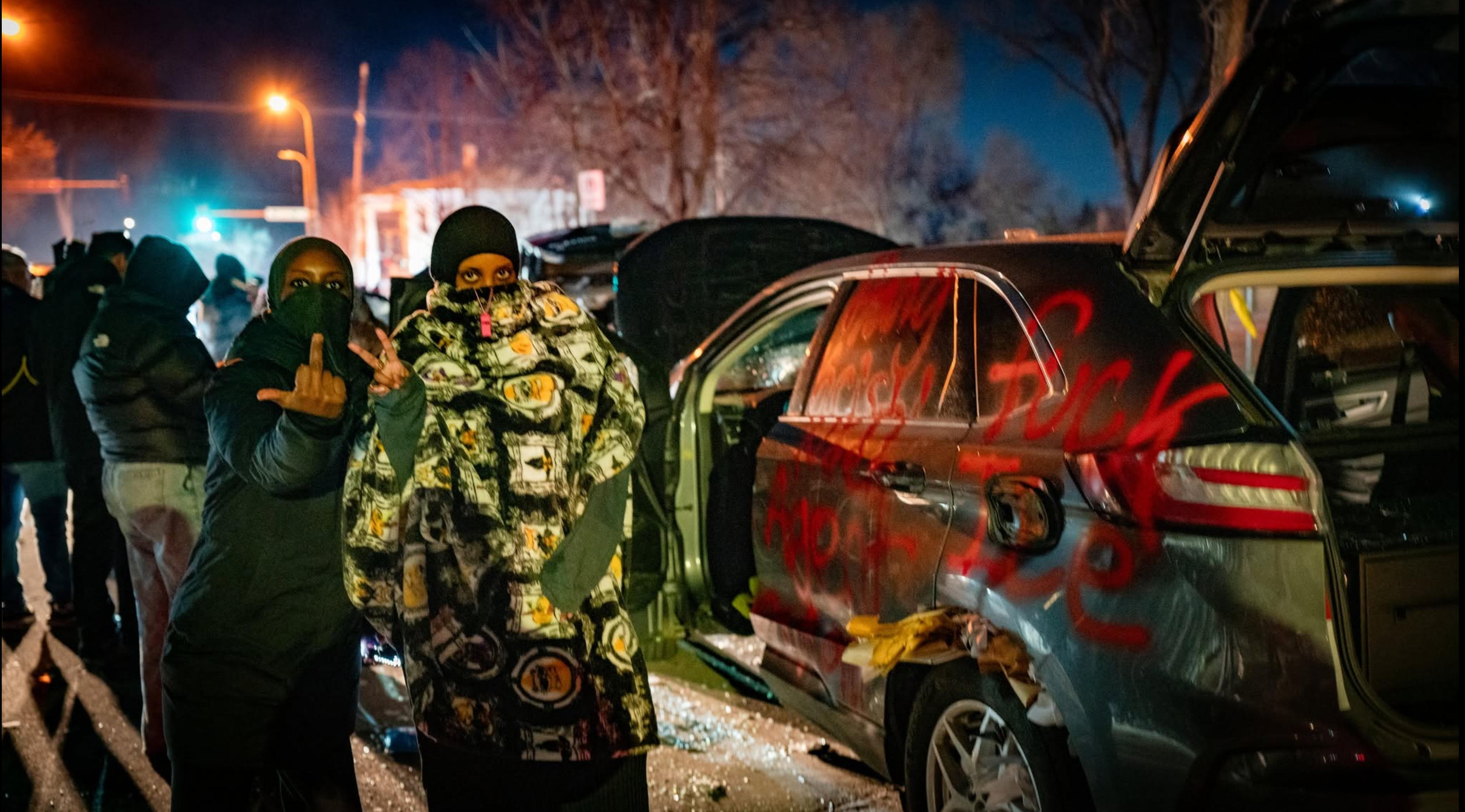 Nighttime street scene with masked people and a damaged vehicle, supplied by the site owner