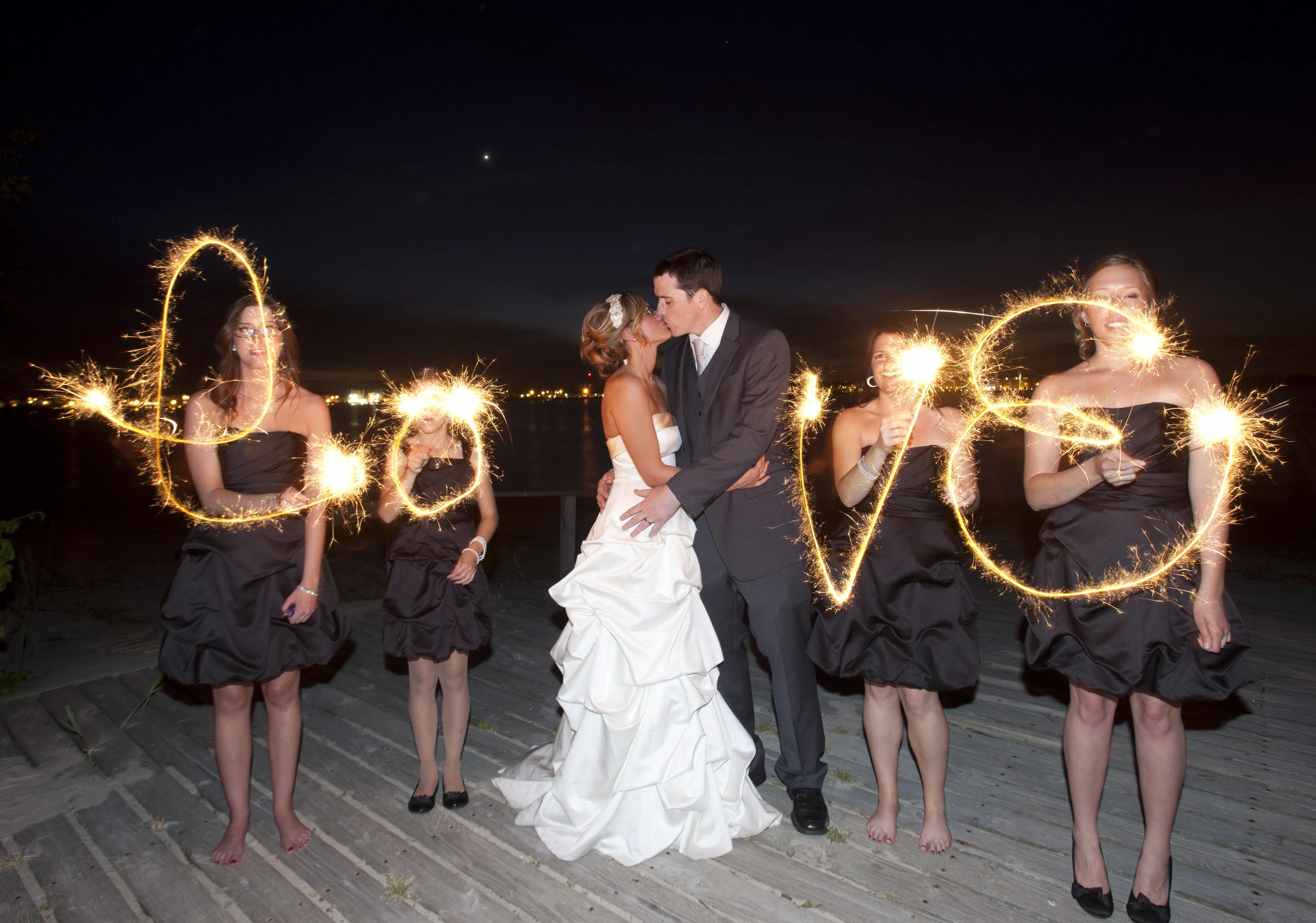 Newlyweds kissing amid sparklers at a waterfront wedding reception