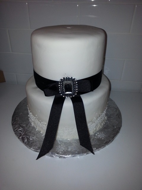 Two-tier white cake with a black ribbon and jeweled buckle