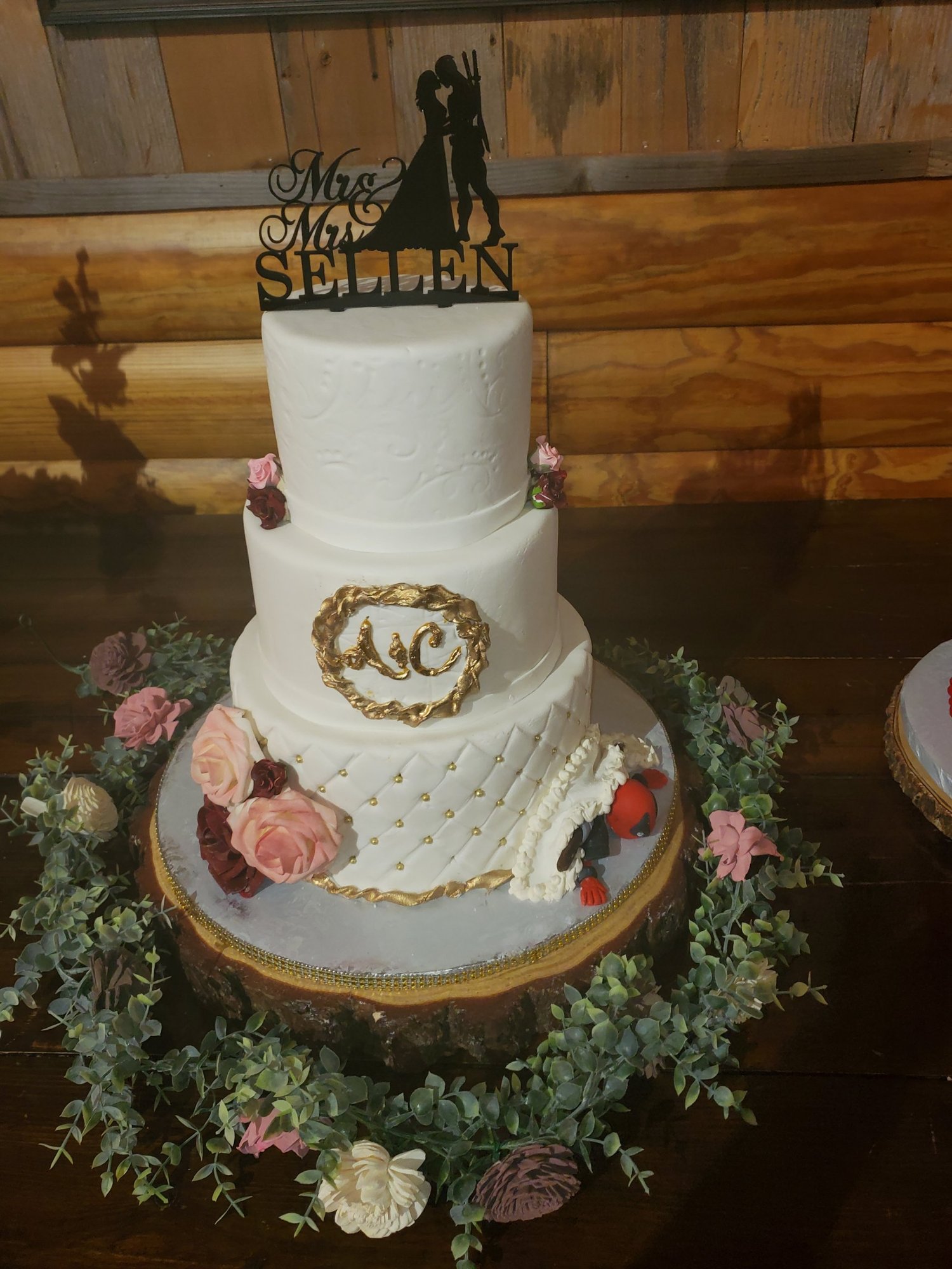 Three-tier white wedding cake with pink flowers, gold details and a silhouette wedding topper