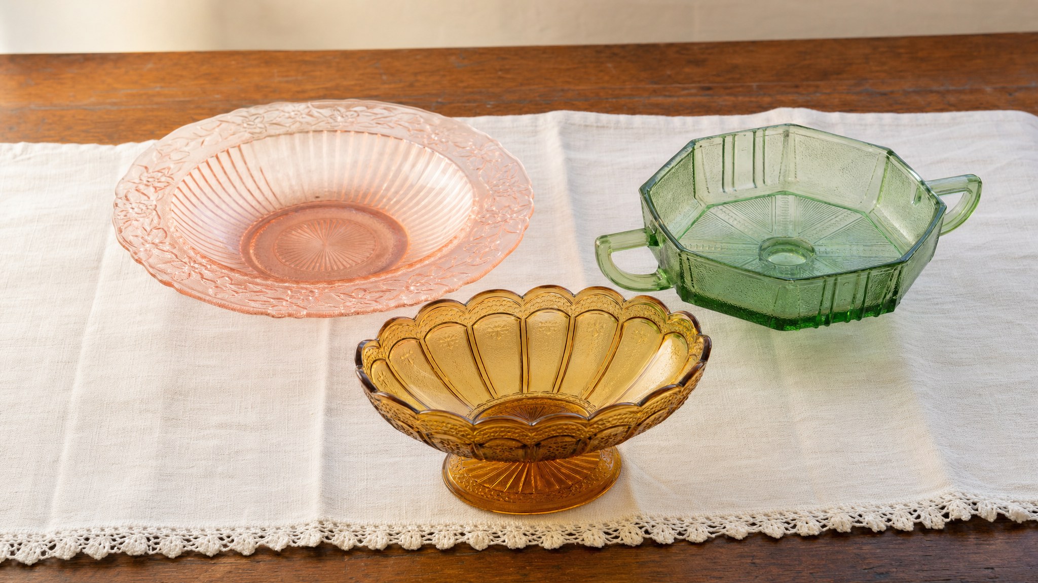 Pink, green, and amber pressed glass pieces arranged on linen