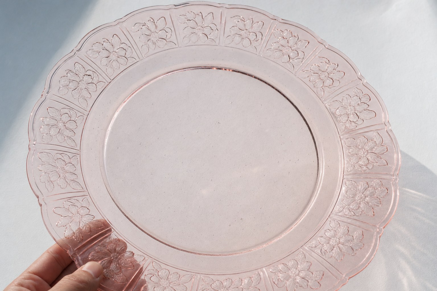 Close view of a pale pink pressed glass plate with repeating floral border
