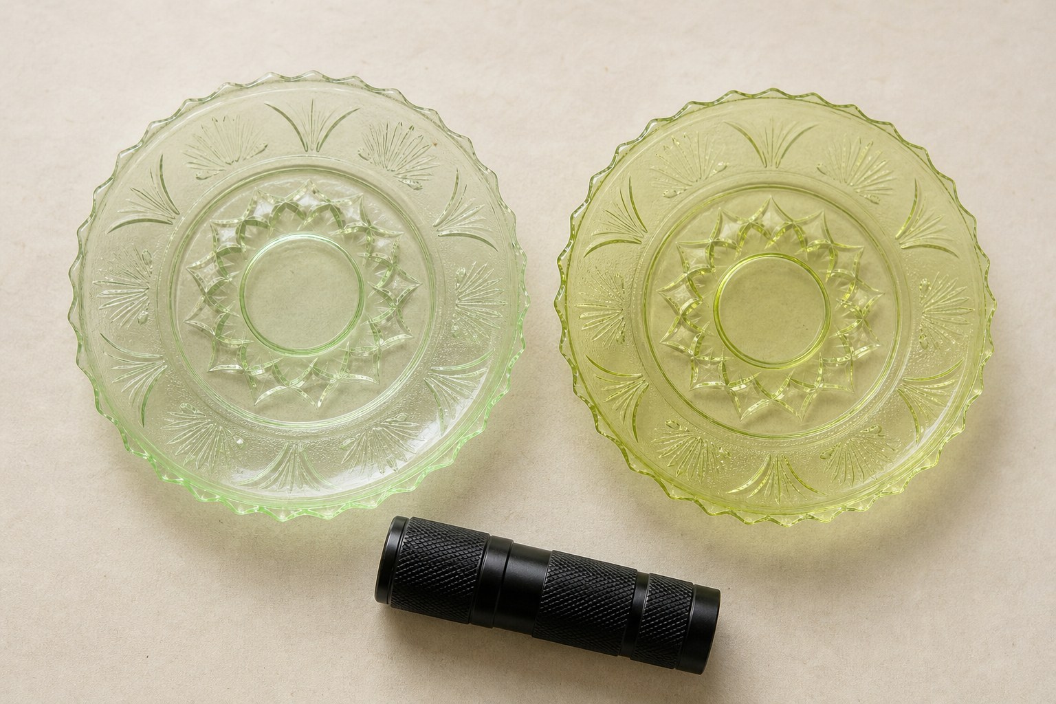 Two pale yellow-green pressed glass saucers in daylight with a small UV flashlight