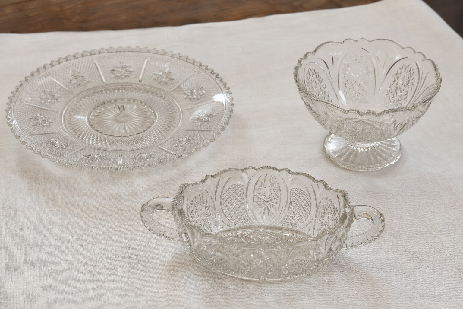 Three distinct pressed-glass forms including a plate, footed bowl, and handled dish