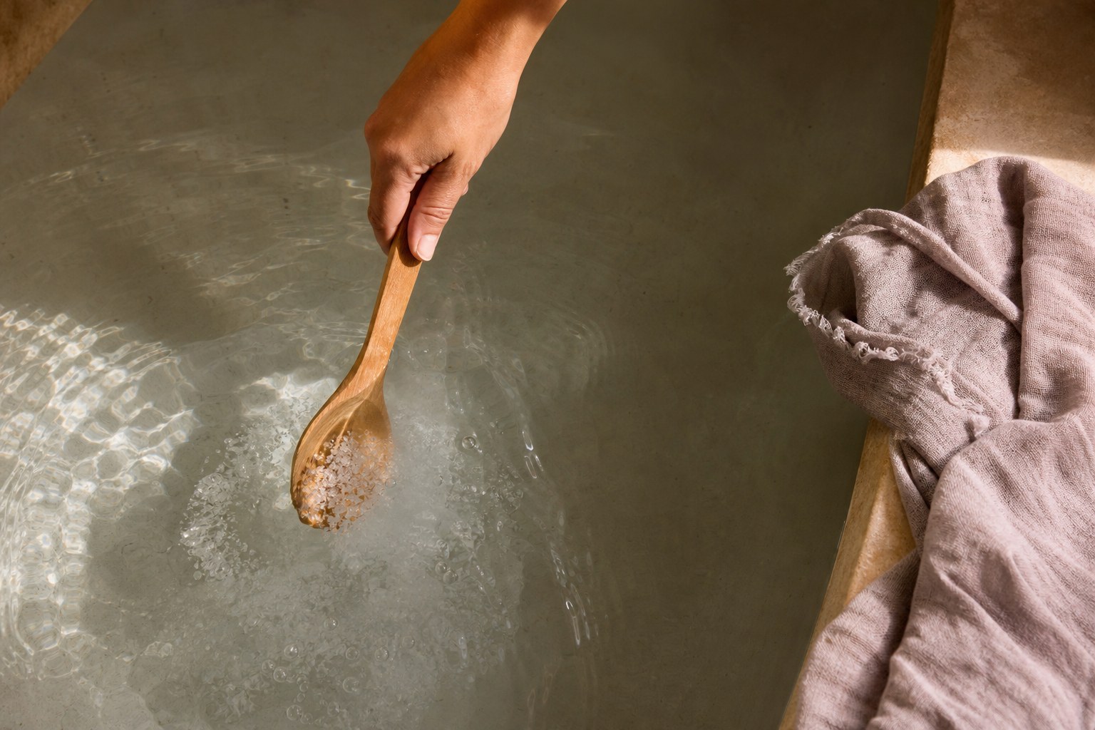 Mineral bath salts dissolving in warm water with a wooden spoon