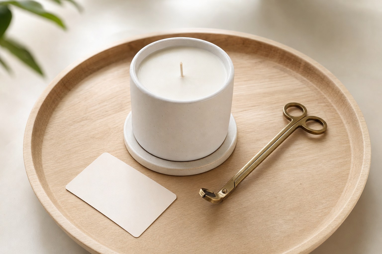 A fully cooled unlit candle on a ceramic coaster beside a wick trimmer on a wooden tray