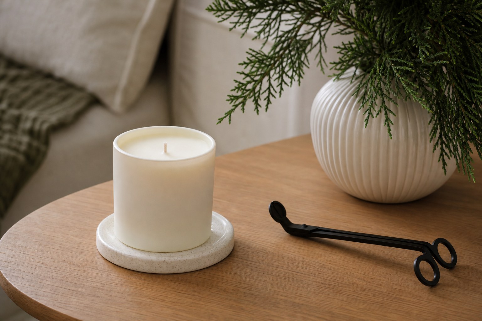 An unlit candle on a ceramic coaster with a wick trimmer nearby