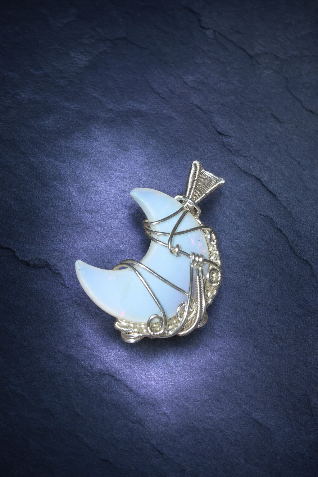 Back of the opalite crescent moon pendant showing the silver overlay wire wrapping on moonlit blue slate