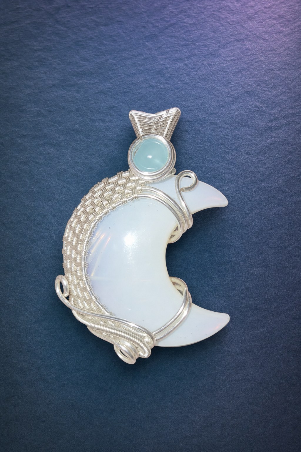 Front of the handmade opalite crescent moon pendant with a blue bead and detailed silver overlay wirework on moonlit blue slate