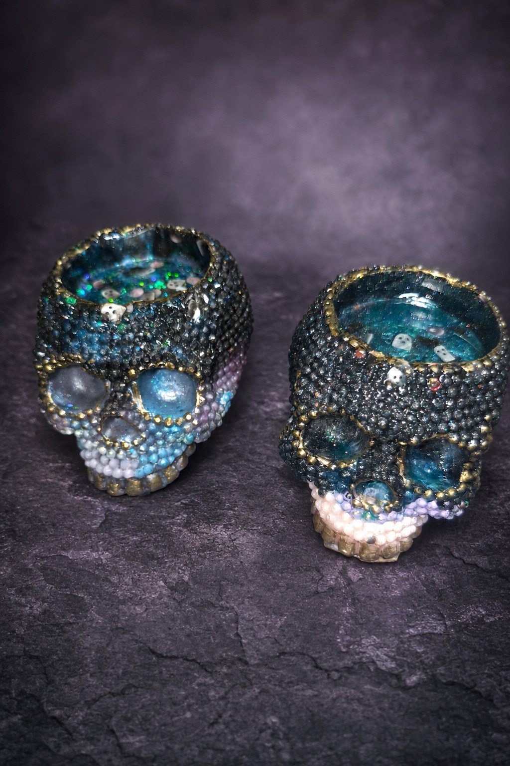 Front view of both resin skull candle holders with gold details and shimmering colors