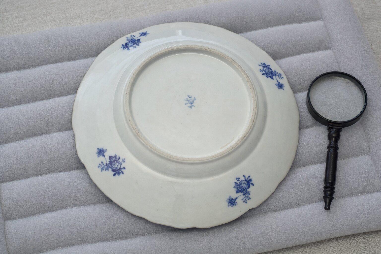 The underside of a decorative porcelain plate beside a magnifier for inspecting its mark