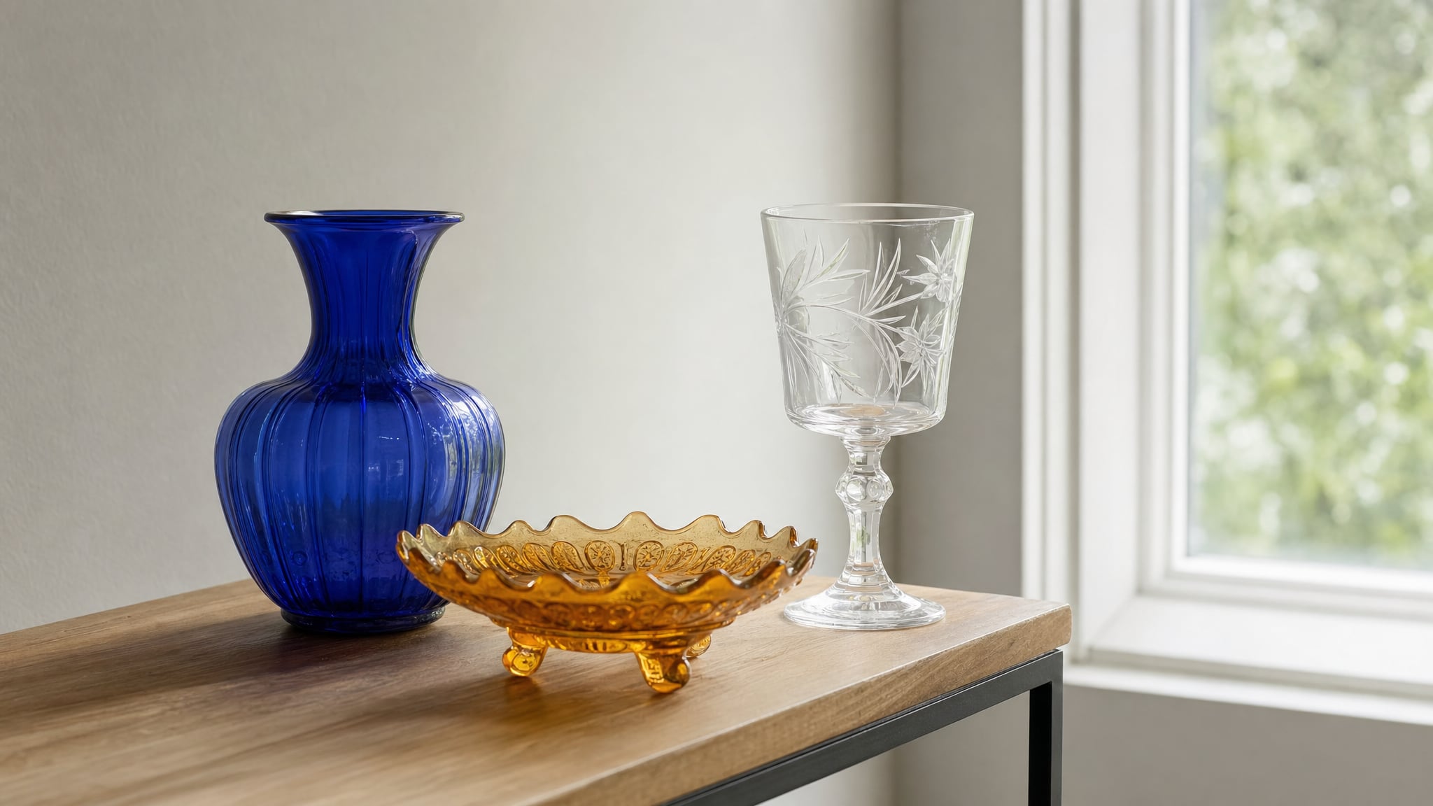 Blue vase, amber dish, and etched goblet displayed near a window