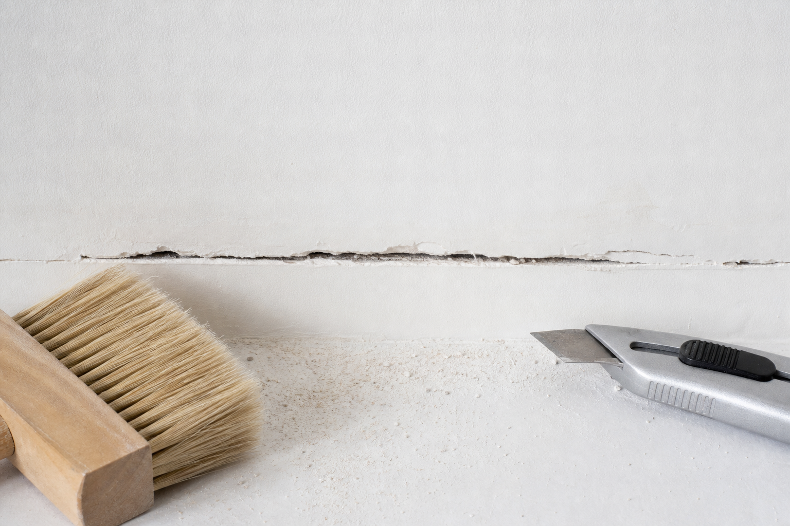 Loose drywall crack material brushed away beside a utility knife