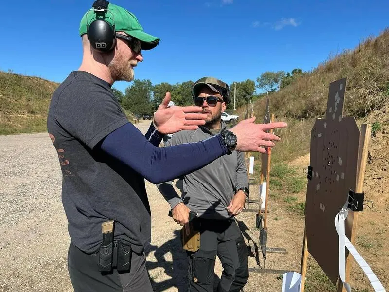 Instructor coaching a student during live-fire pistol training on an outdoor range