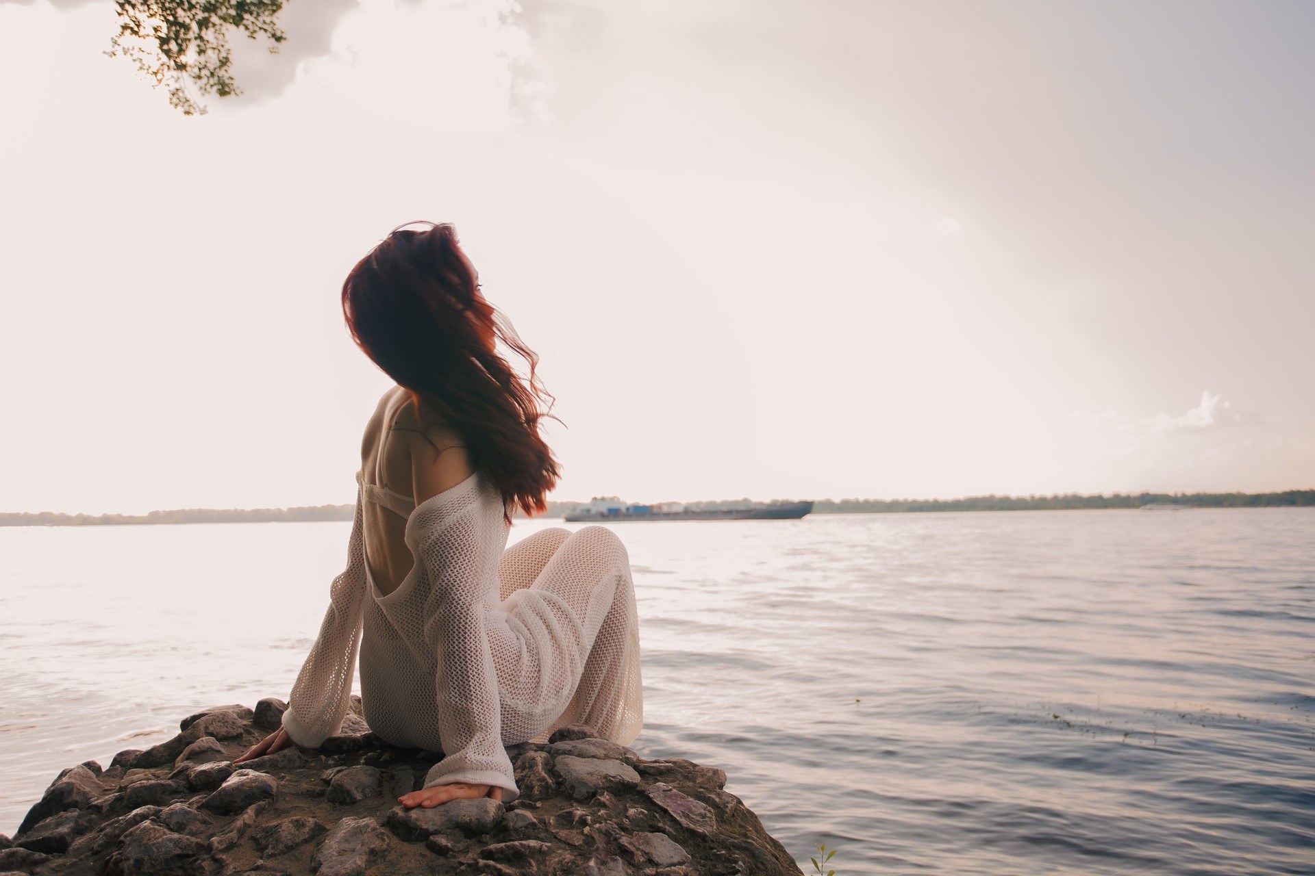 Woman sitting on rocks beside calm water