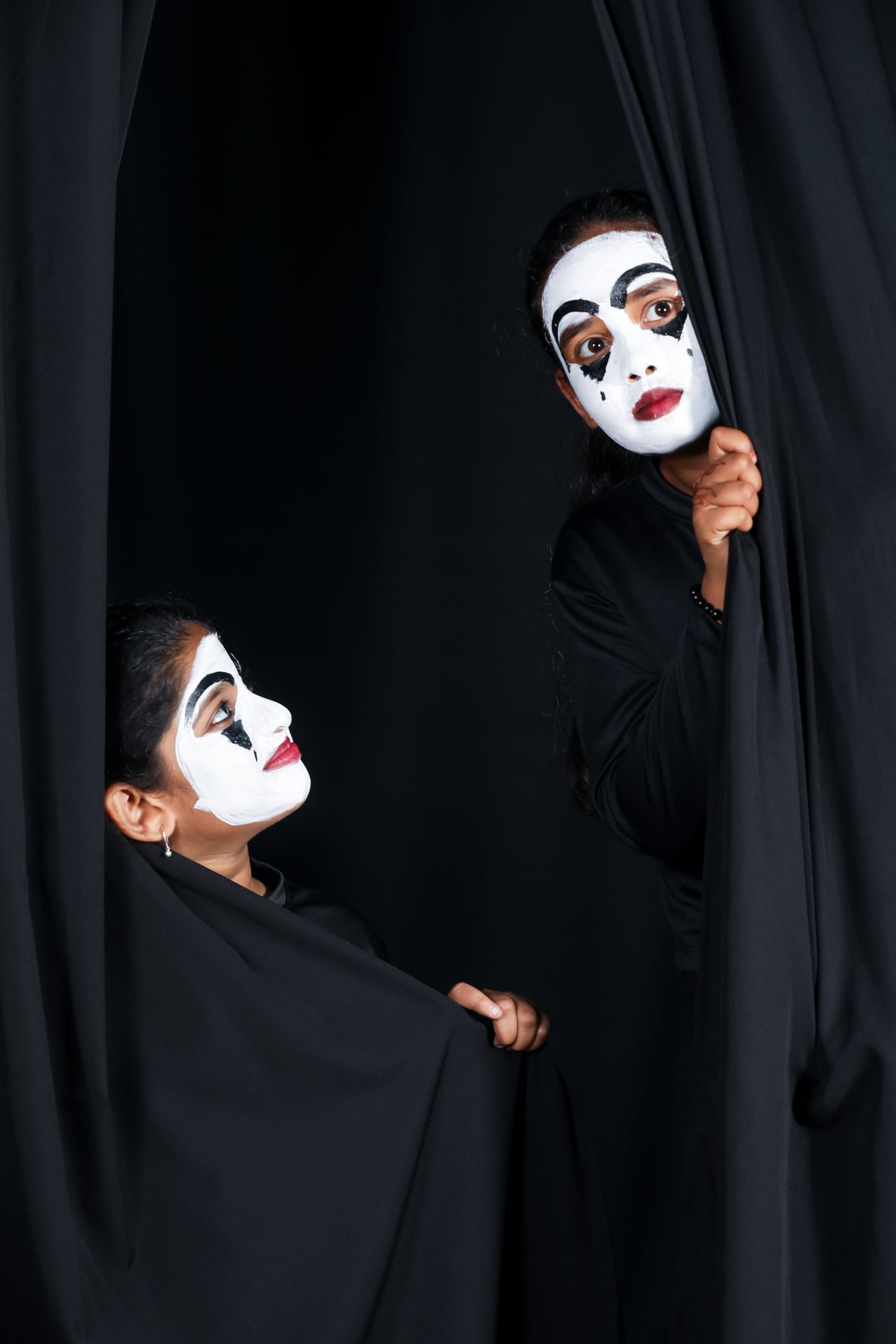 Two performers in theatrical makeup looking out from behind stage curtains