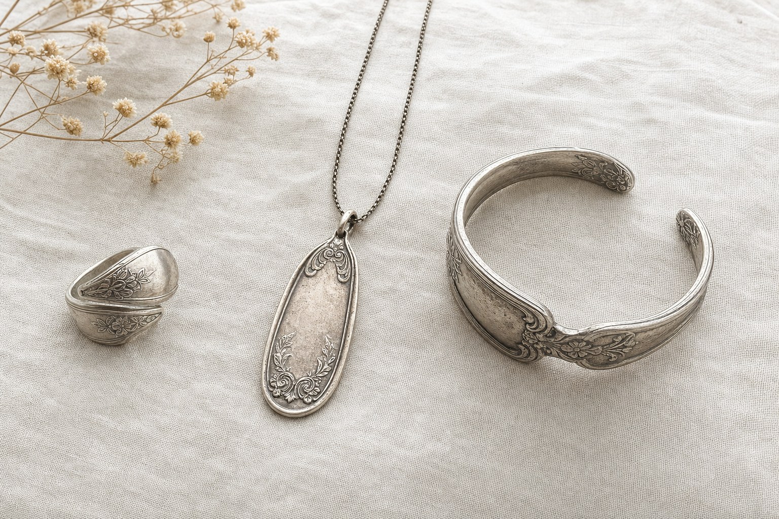 Silverware-inspired ring, pendant, and cuff arranged on cream linen