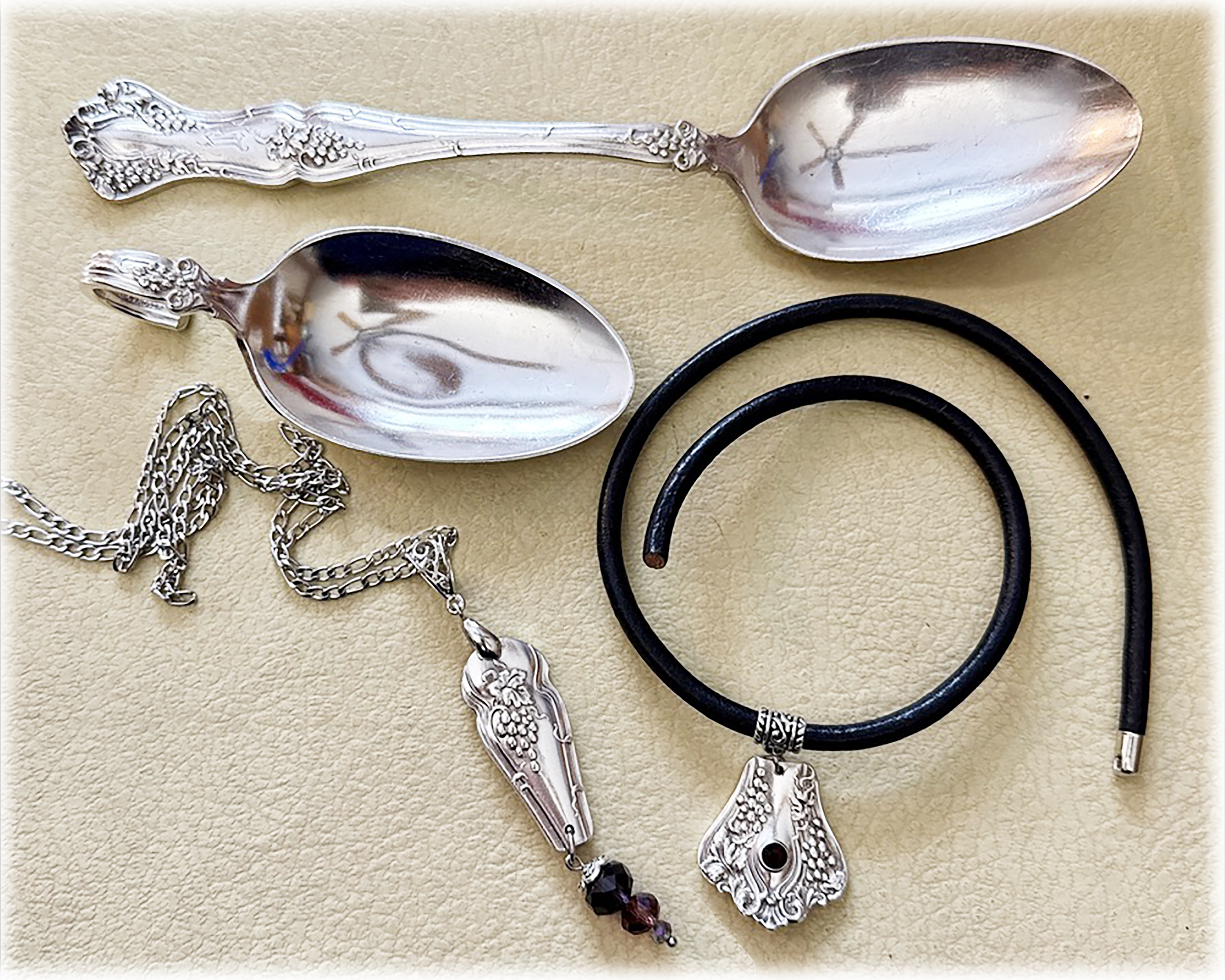 Vintage grape-pattern spoons beside matching custom necklace and leather cord pendant