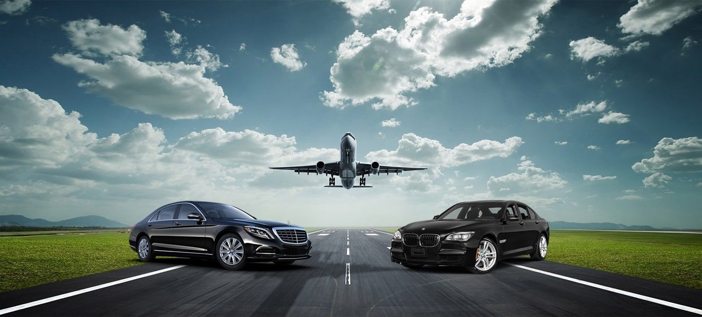 Two black luxury sedans at an airport with an aircraft overhead
