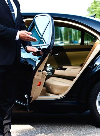 Chauffeur welcoming a passenger into a luxury sedan