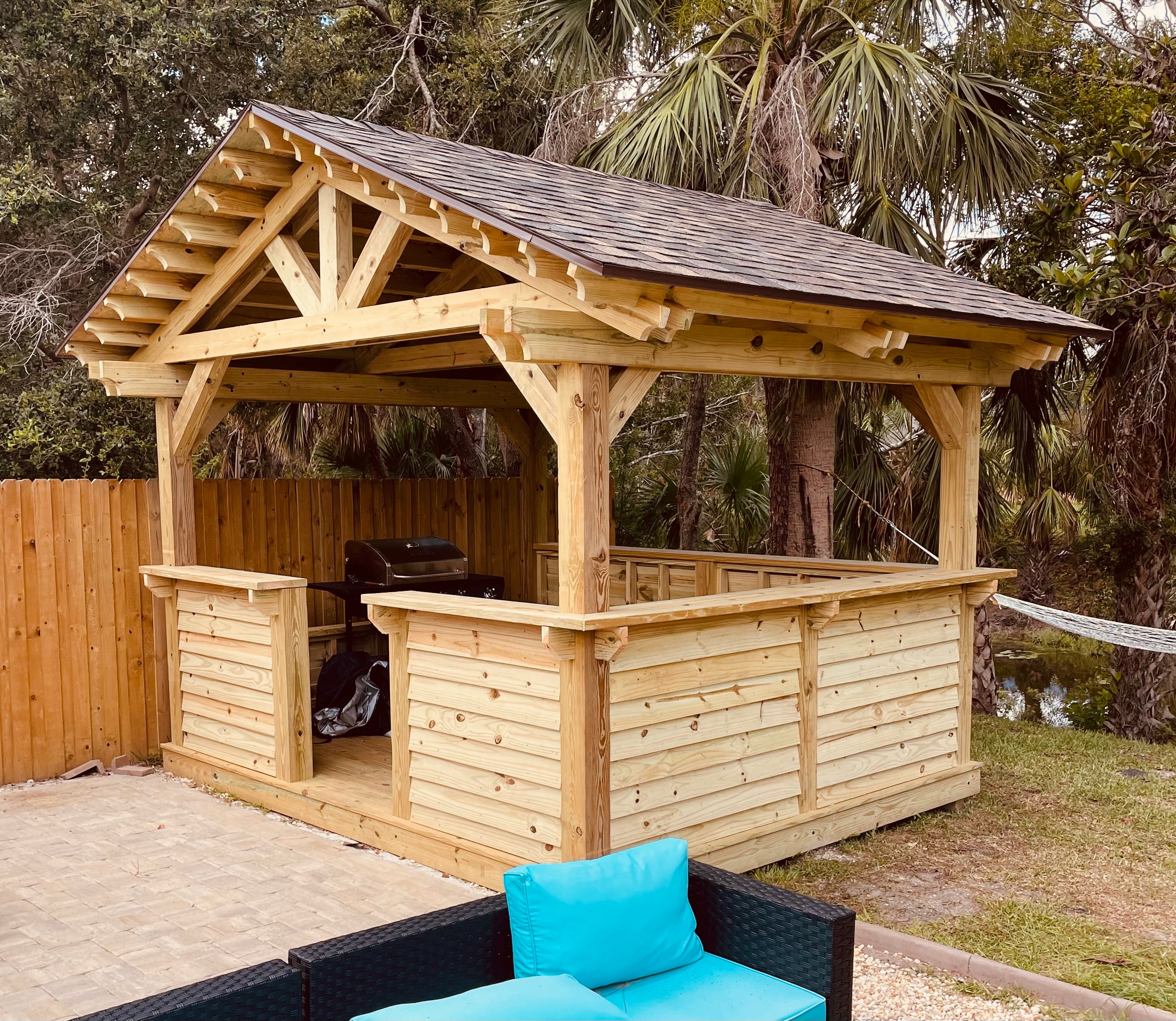 Wooden backyard gazebo with a shingled roof and outdoor grill