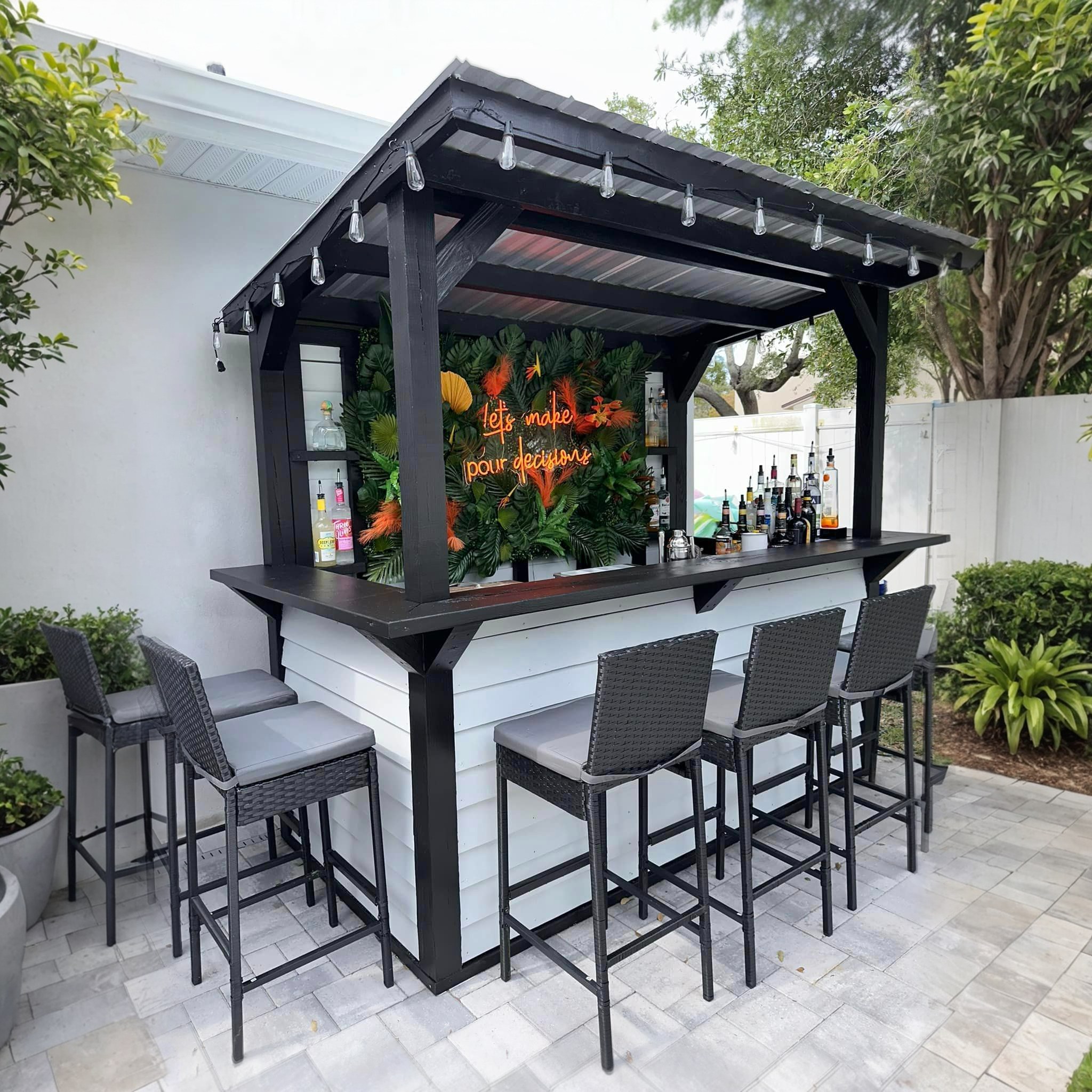 A finished custom backyard bar with black framing, stools and tropical planting