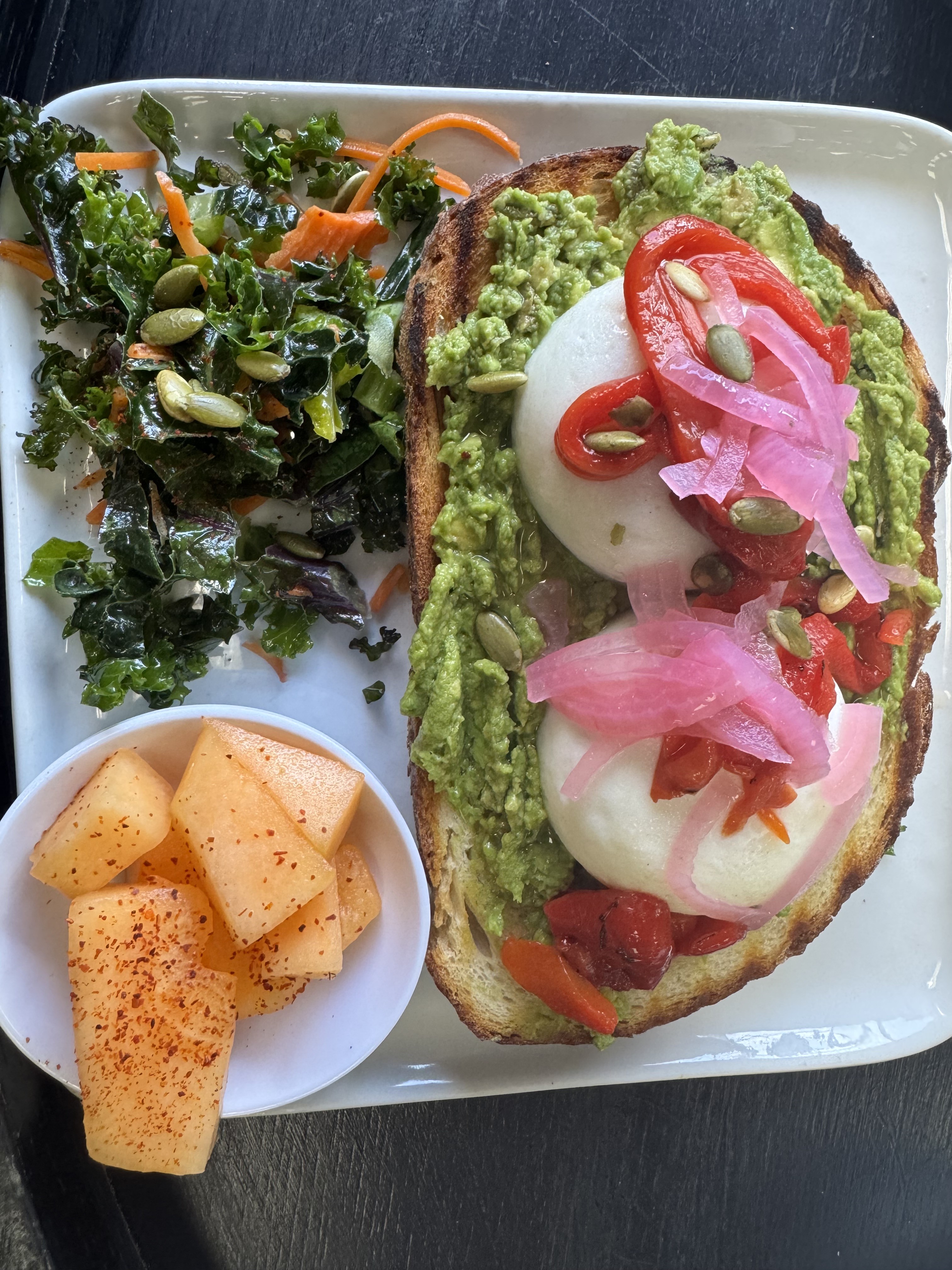 Avocado toast with poached eggs, pickled onion, kale salad, and chili-dusted cantaloupe