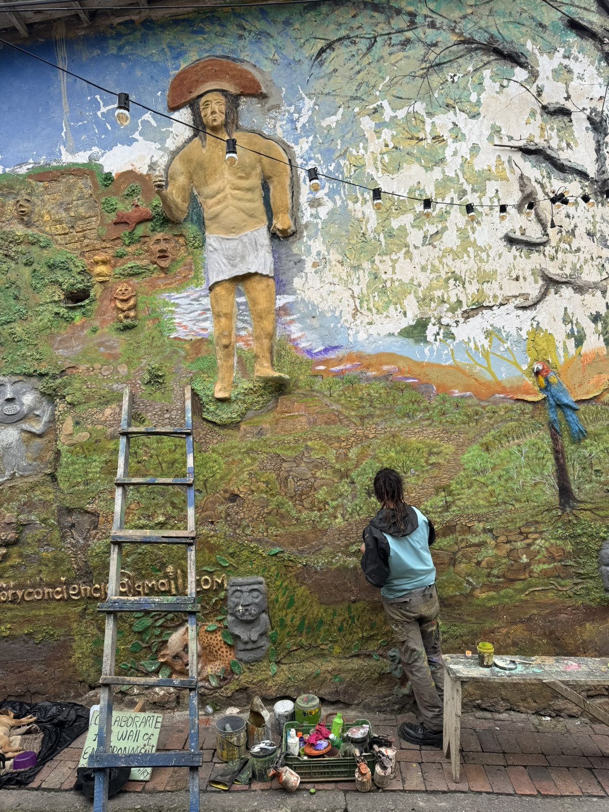 Street artist painting a mural from a ladder in La Candelaria