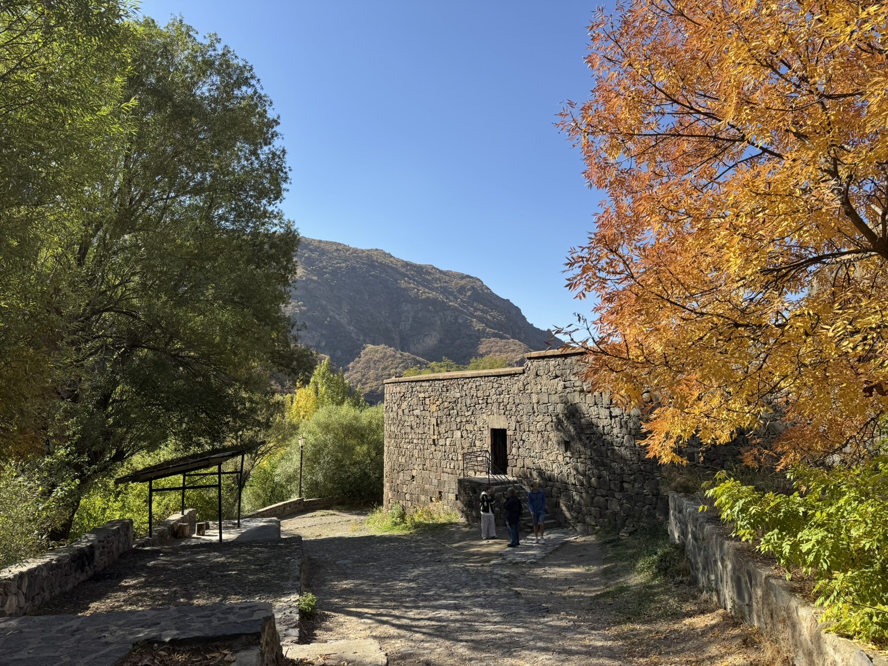 Autumn trees beside the stone buildings of Geghard Monastery.