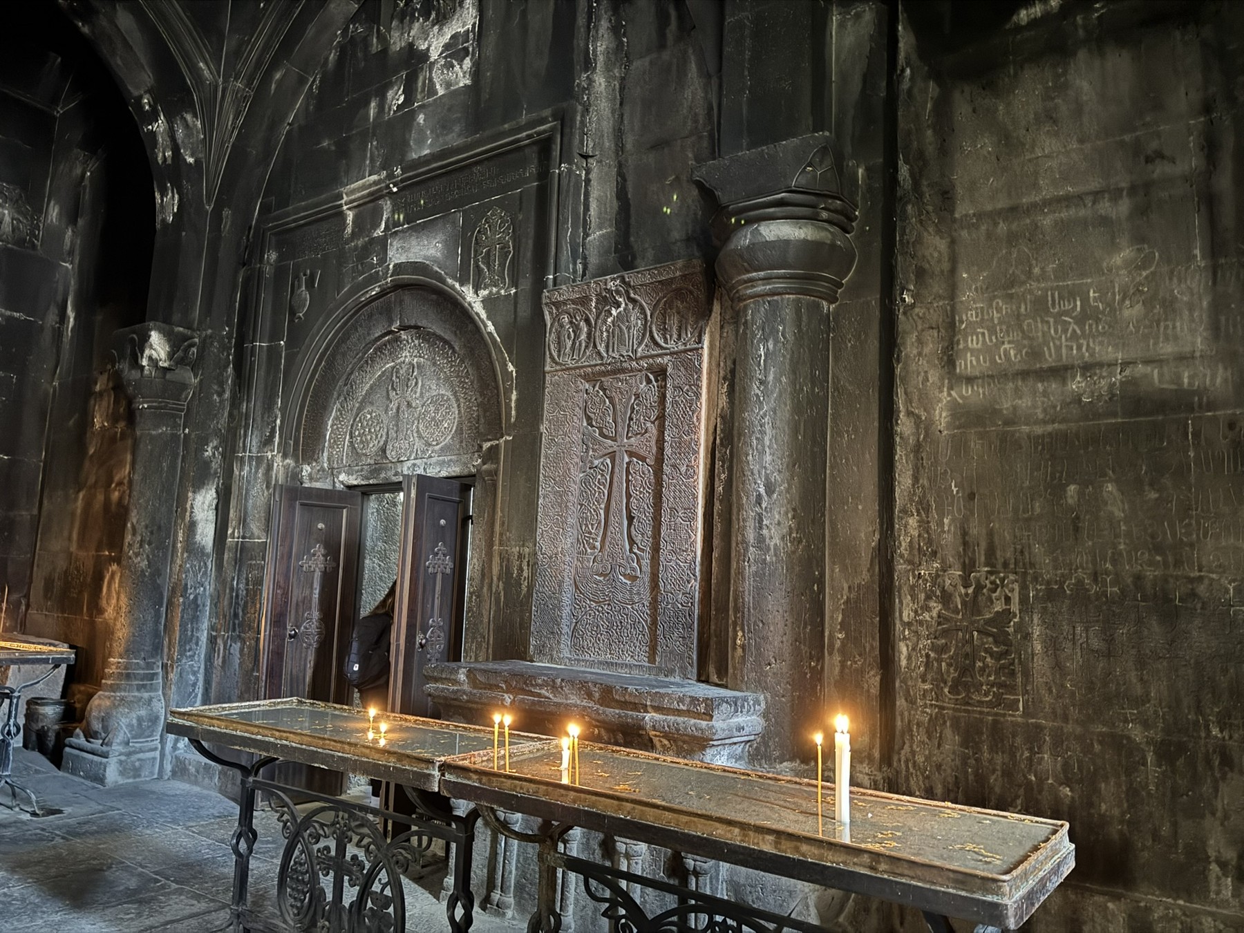 Candles beneath carved arches and crosses inside Geghard Monastery.