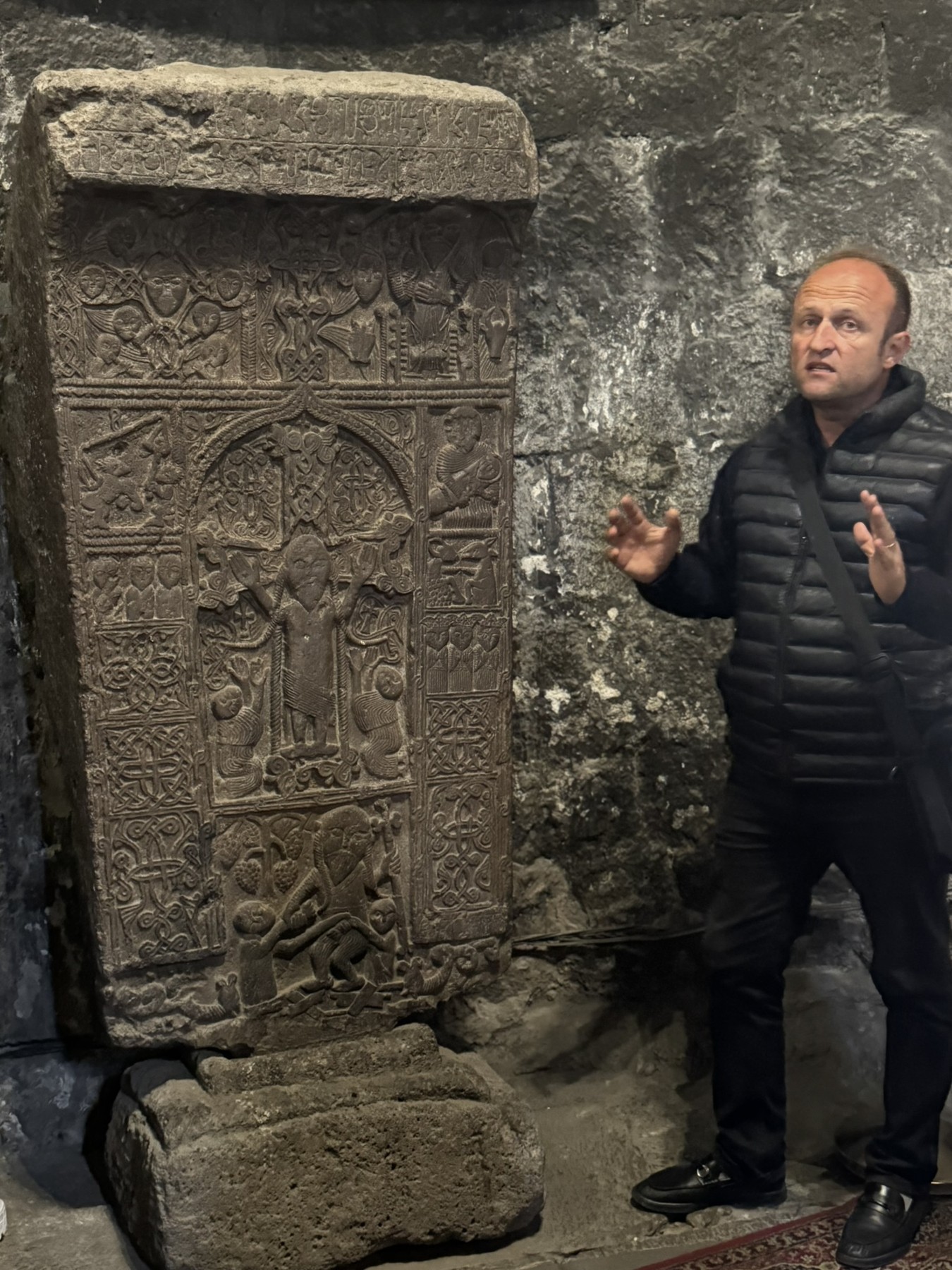 A guide beside a carved Armenian cross-stone inside Geghard Monastery.