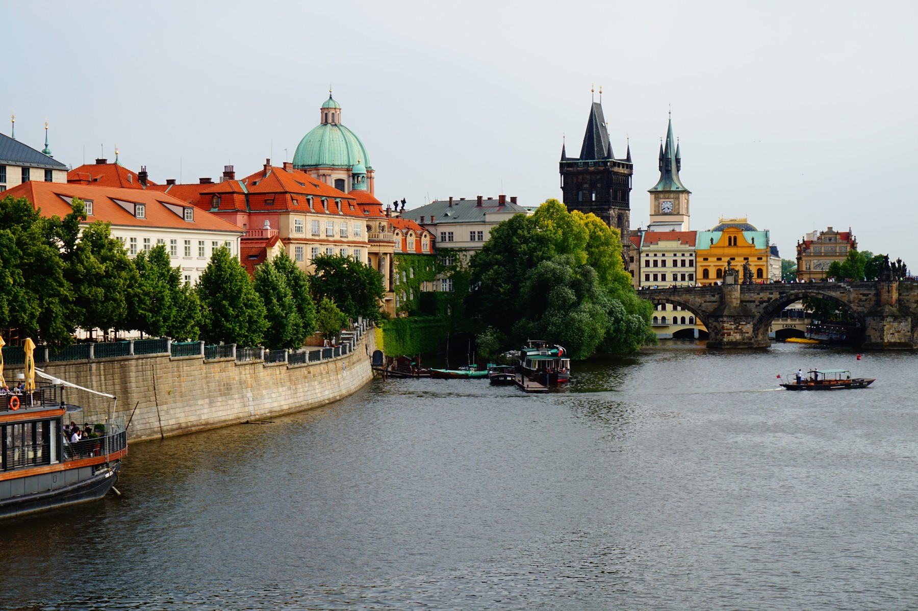 The Vltava River with boats and historic Prague buildings along its banks.